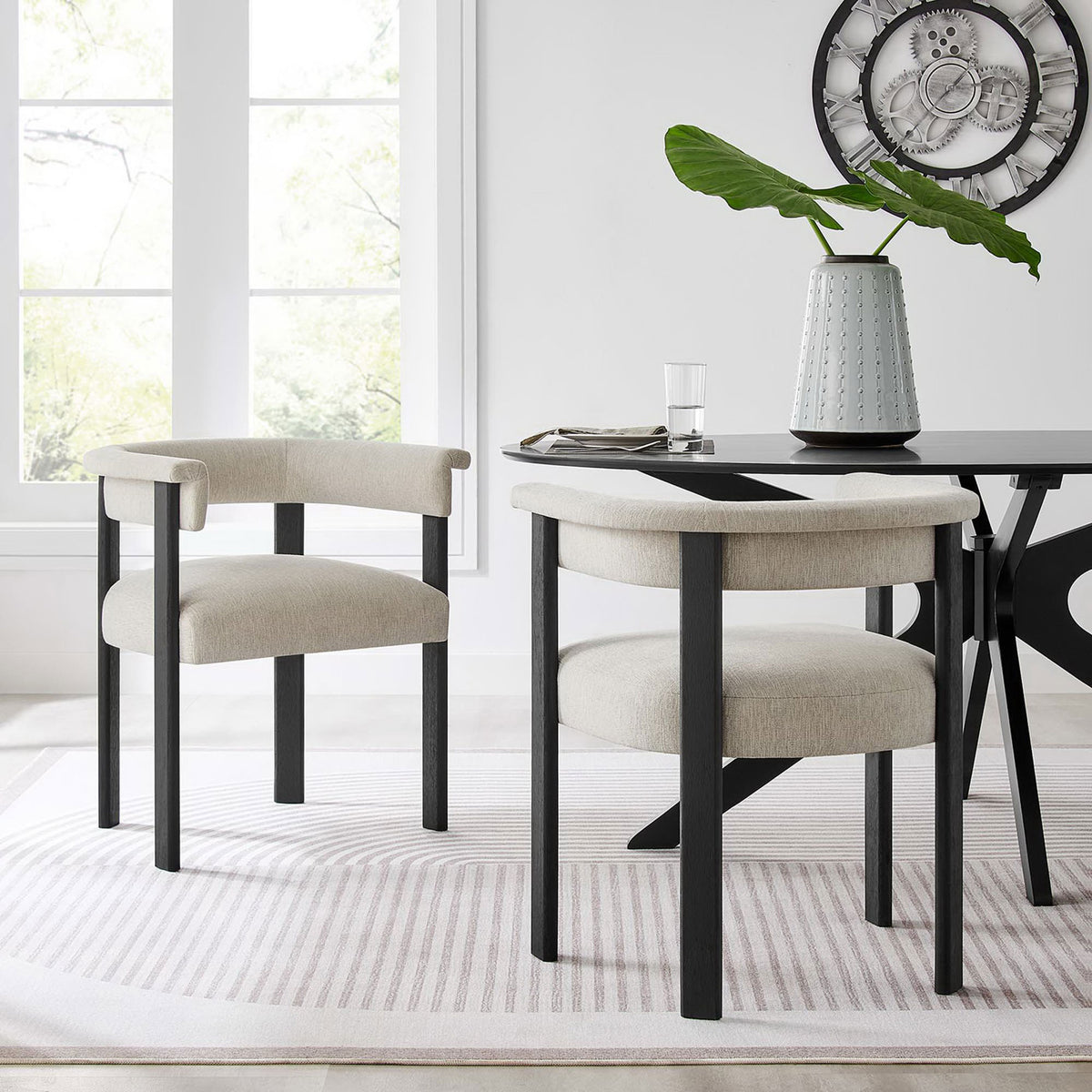 Pair of Imogen barrel dining chairs frame a sleek dining table in a bright contemporary room || EEI-6776-HEI-BLK || front_angle_multi_room