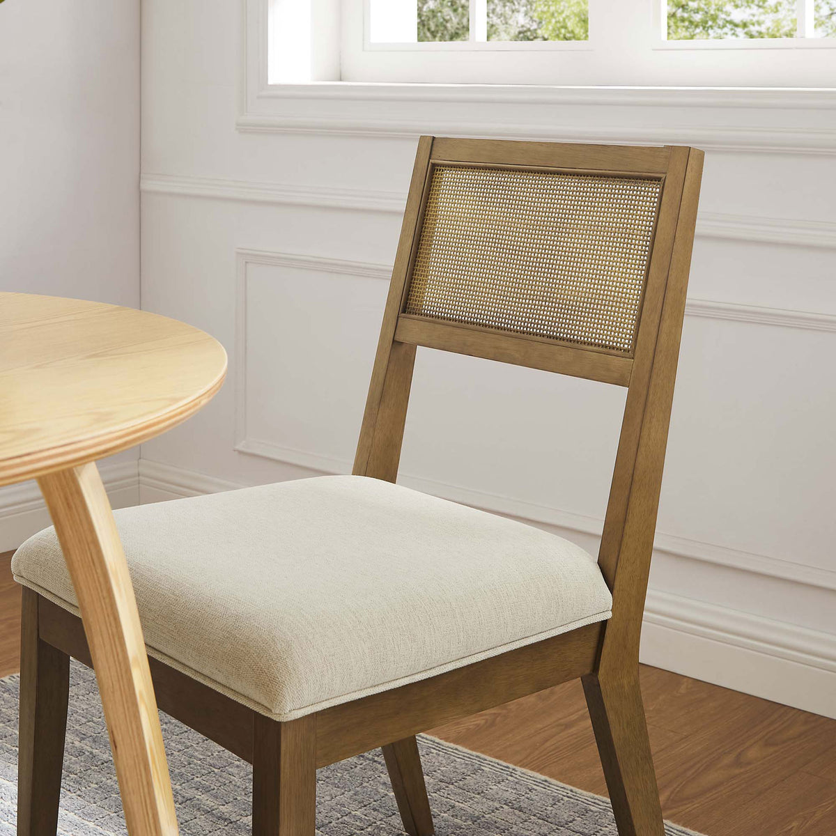 Cane back dining chair with ivory seat styled beside a round wood table in a bright room || EEI-6781-FRO-HEI || front_angle_room