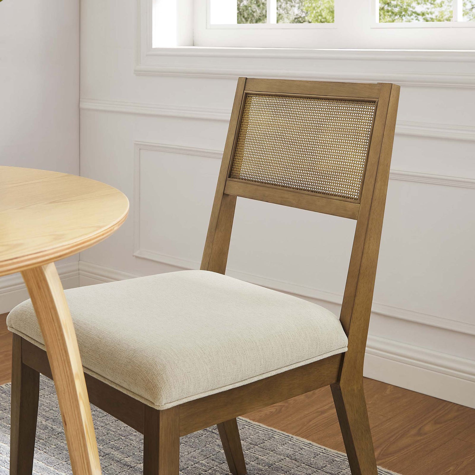 Cane back dining chair with ivory seat styled beside a round wood table in a bright room || EEI-6781-FRO-HEI || front_angle_room