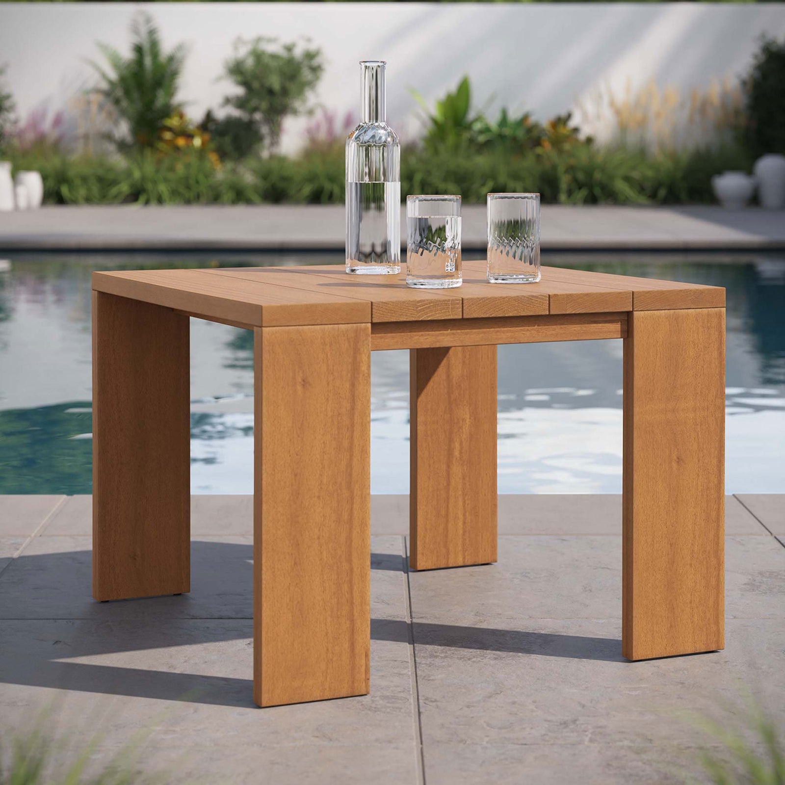Acacia wood side table styled with glassware by the pool, adding warm modern charm to outdoor seating. || EEI-6787-NAT || front_angle_room
