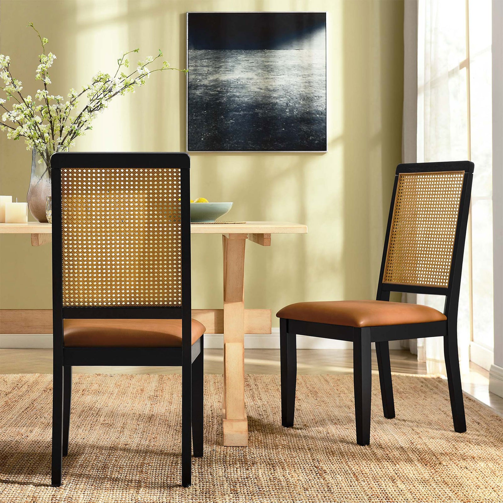 Pair of Arlo dining chairs around a light wood table on a woven rug in a modern dining room || EEI-6802-BLK-NAT-TAN || back_angle_multi_room
