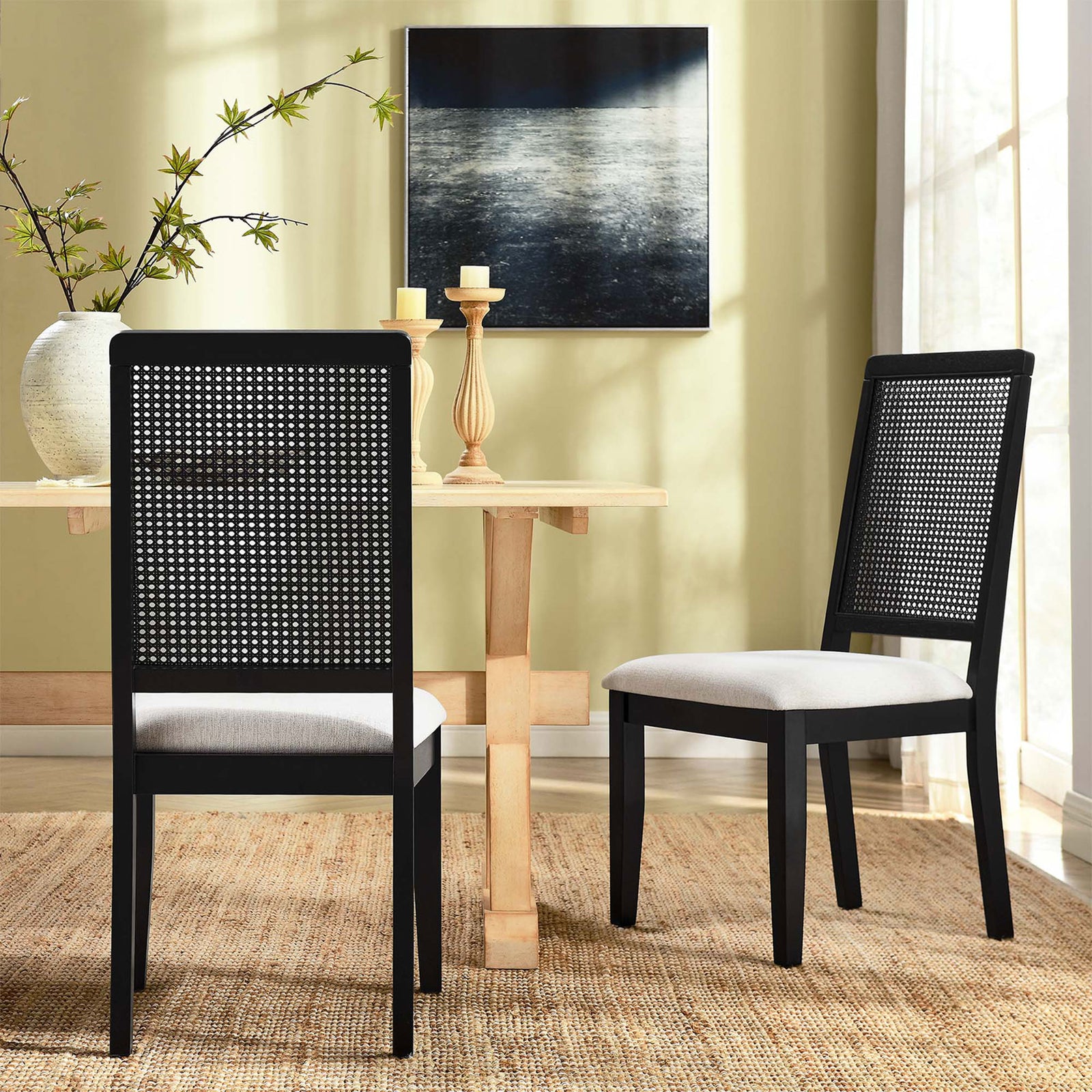 Two black faux rattan dining chairs with ivory cushions styled around a light wood dining table || EEI-6803-BLK-BLK-HEI || back_angle_multi_room