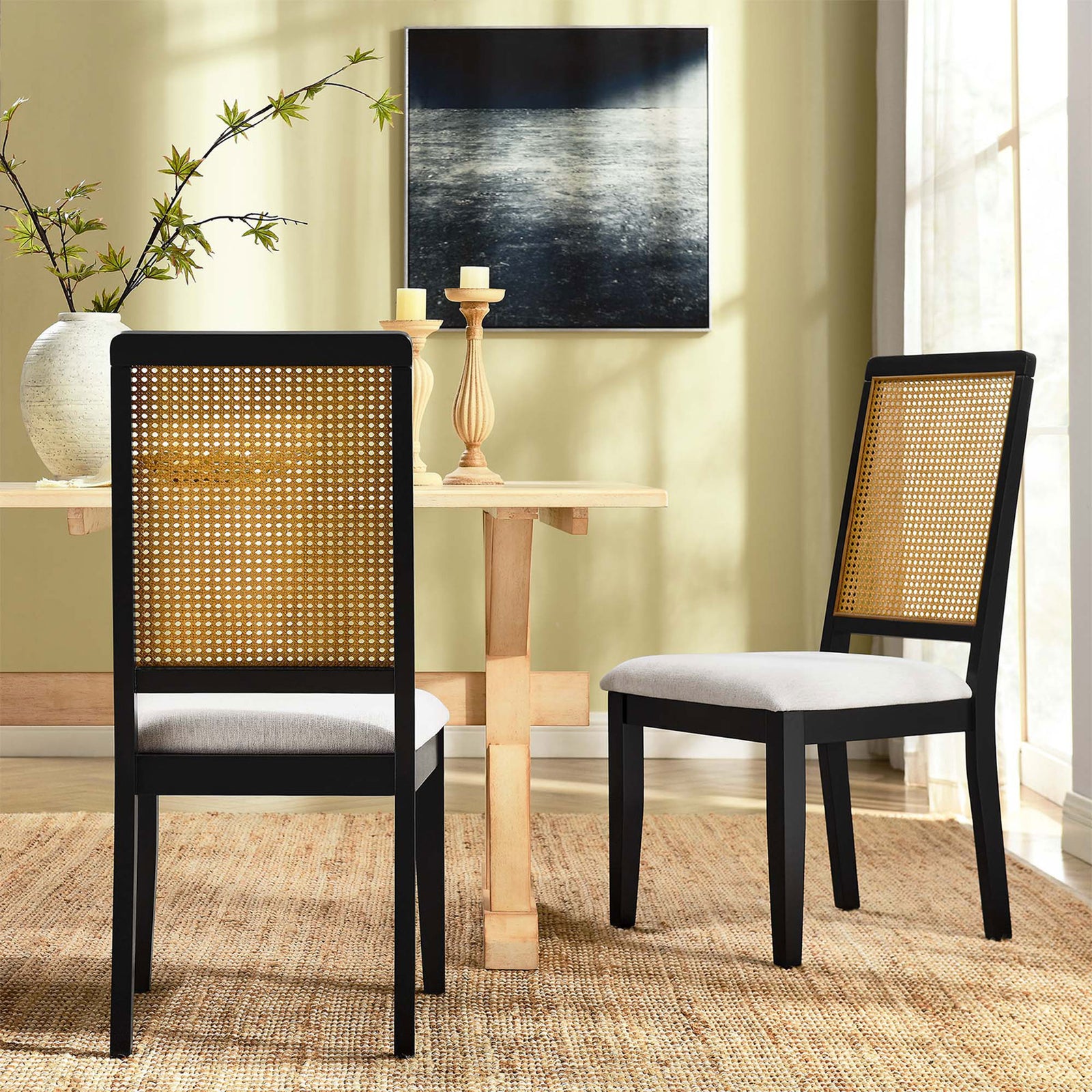 Pair of black and natural cane dining chairs with ivory seats gathered around a light wood table || EEI-6803-BLK-NAT-HEI || front_angle_multi_room