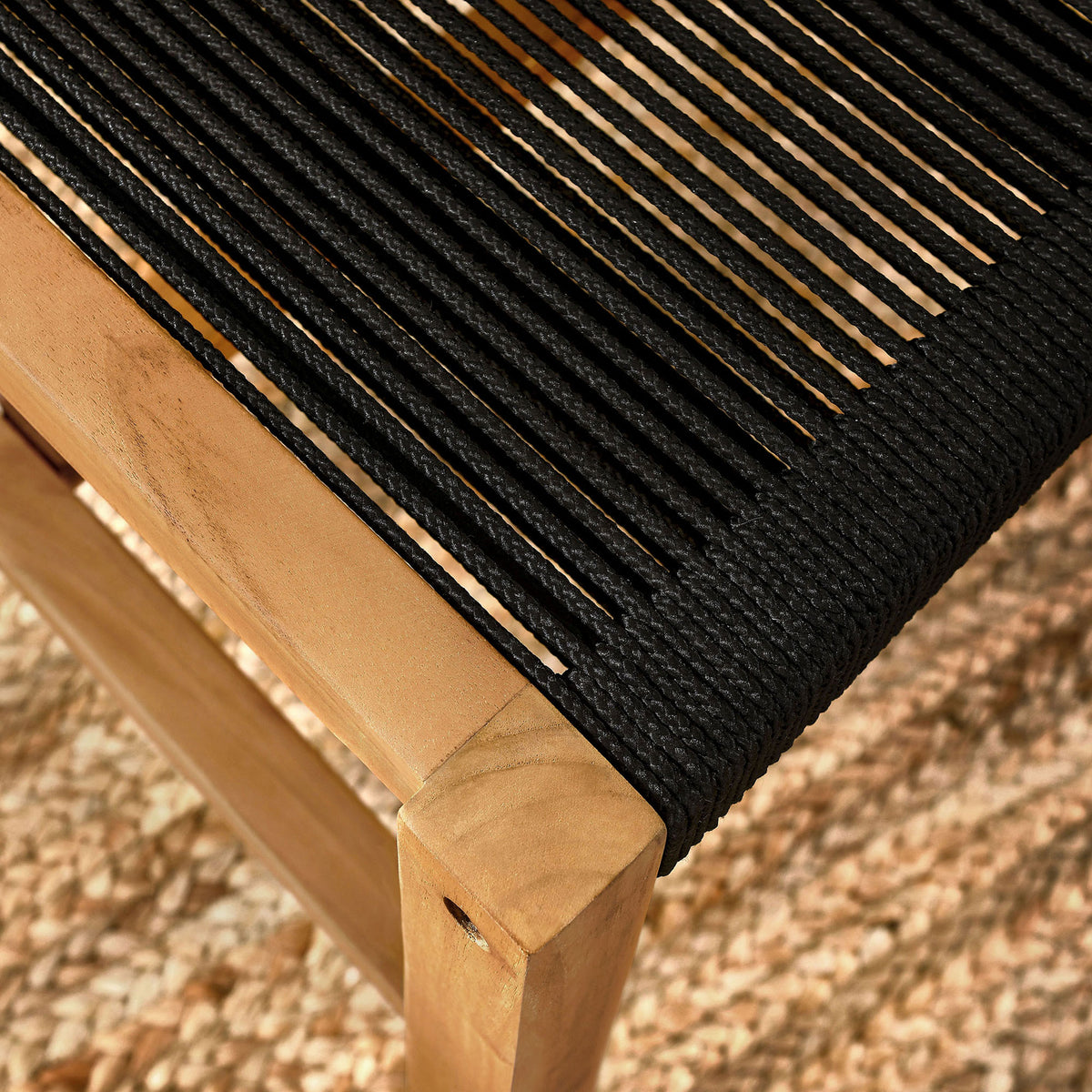 Sunlit black rope seat and teak frame sit over a textured outdoor rug for relaxed coastal dining || EEI-6805-NAT-BLK || detail_room