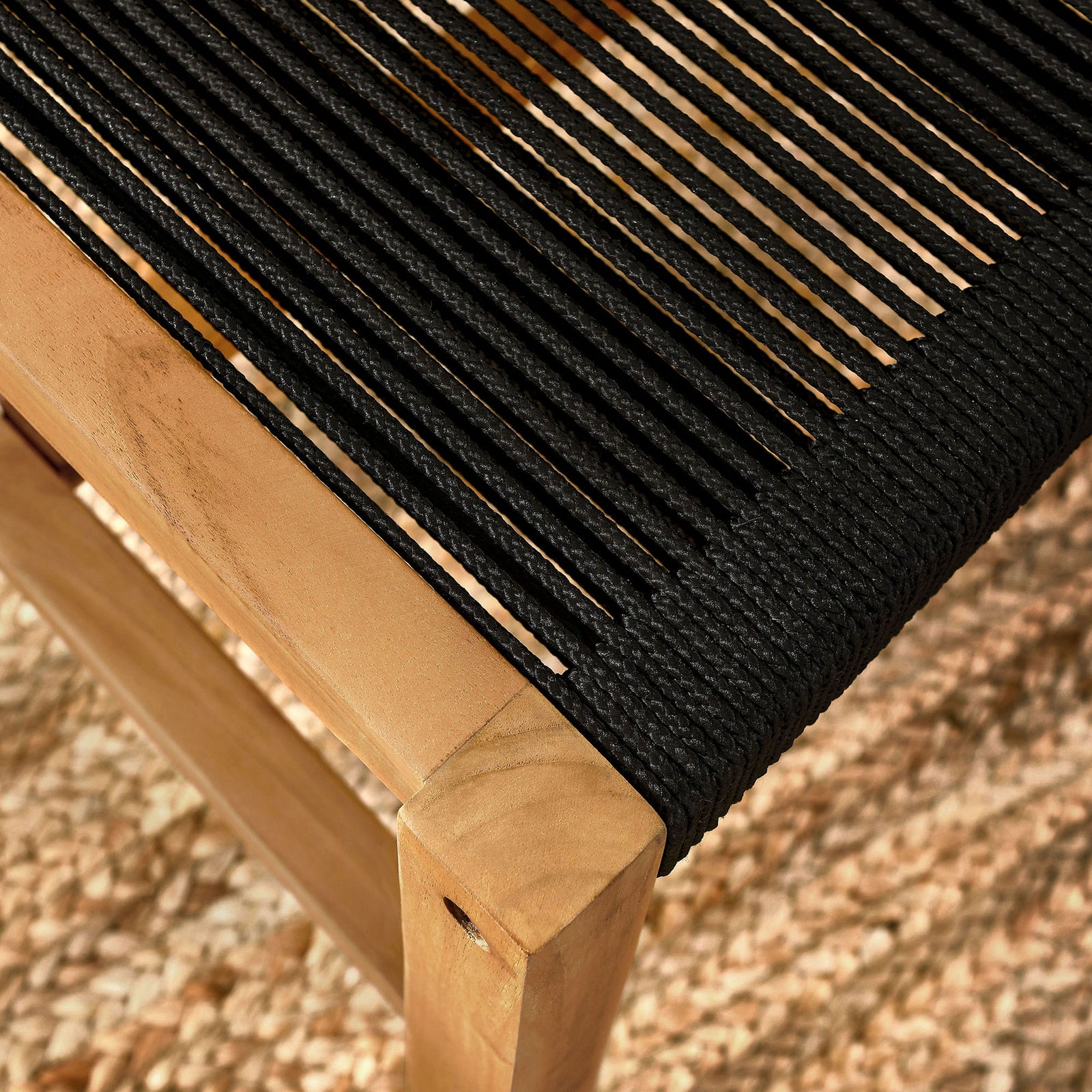 Sunlit black rope seat and teak frame sit over a textured outdoor rug for relaxed coastal dining || EEI-6805-NAT-BLK || detail_room