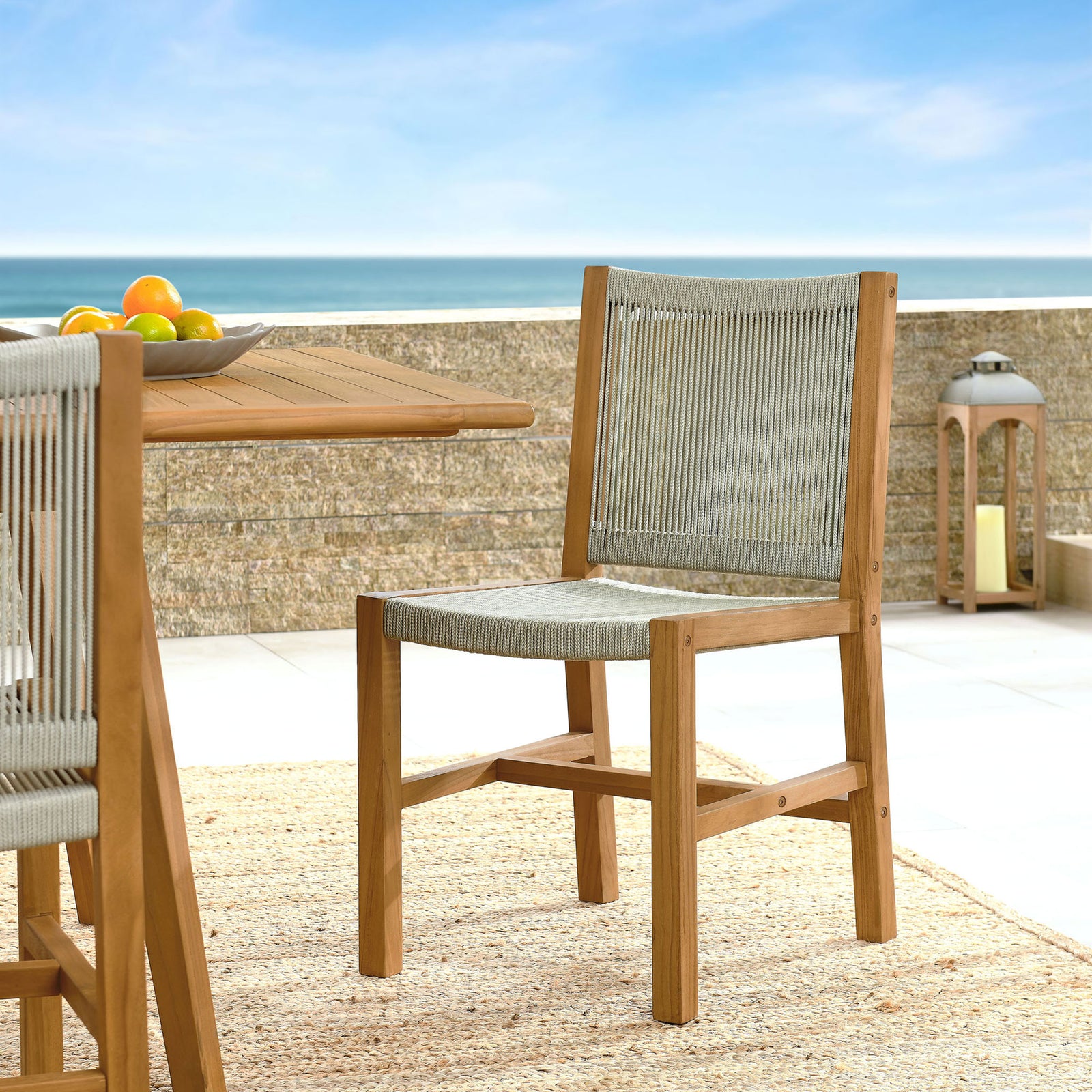 Teak and natural rope dining chair styled beside a coastal table on a bright outdoor terrace || EEI-6805-NAT-NAT || front_angle_room