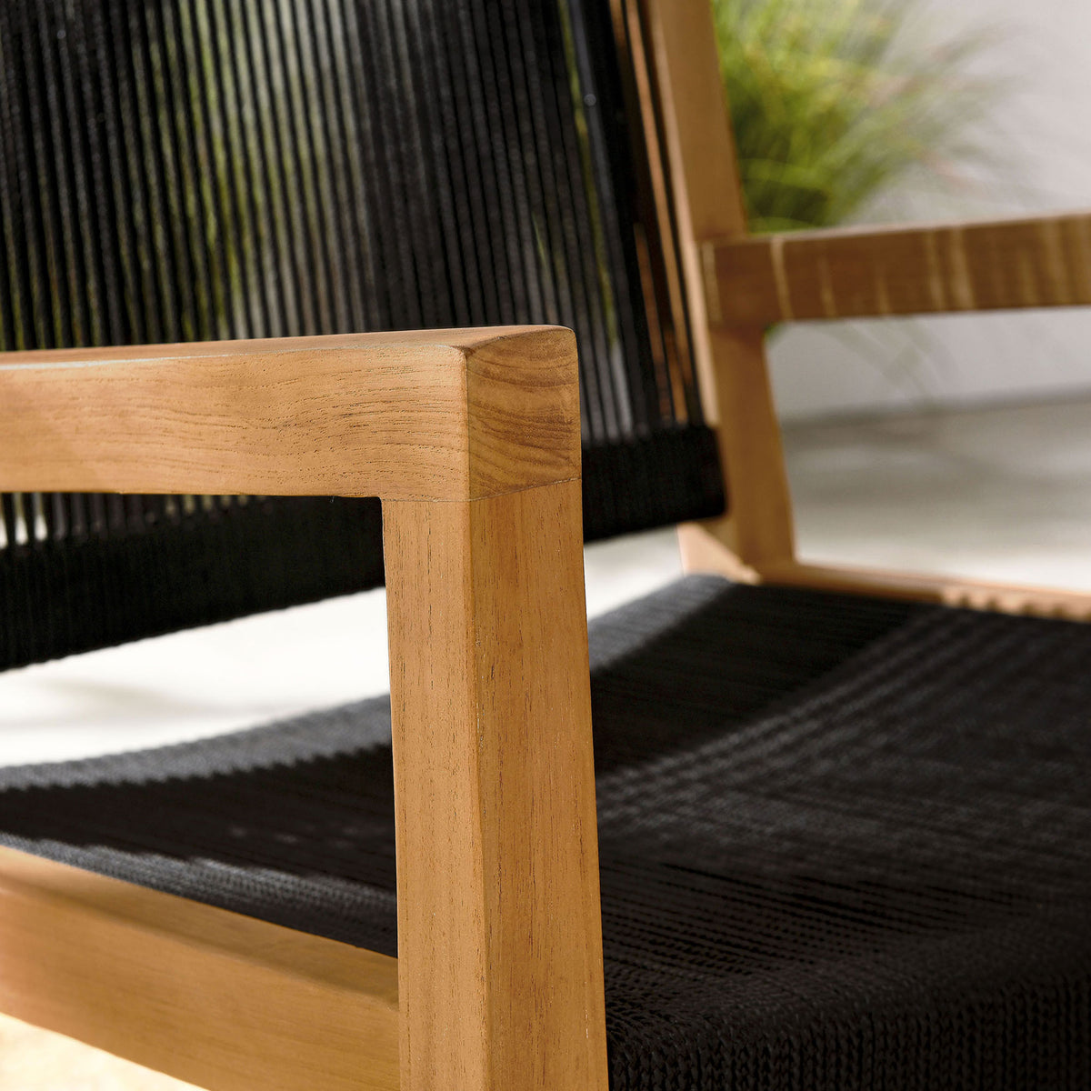 Teak arm and black rope seat catch sunlit texture, blending with relaxed coastal patio decor || EEI-6806-NAT-BLK || detail_room