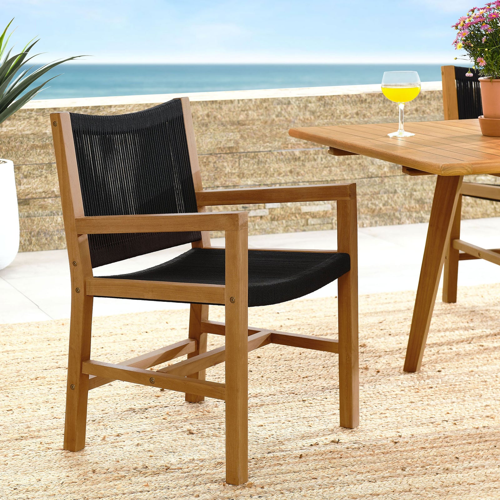 Teak and black rope armchair styled on a sunny patio next to matching teak dining table || EEI-6806-NAT-BLK || front_angle_room