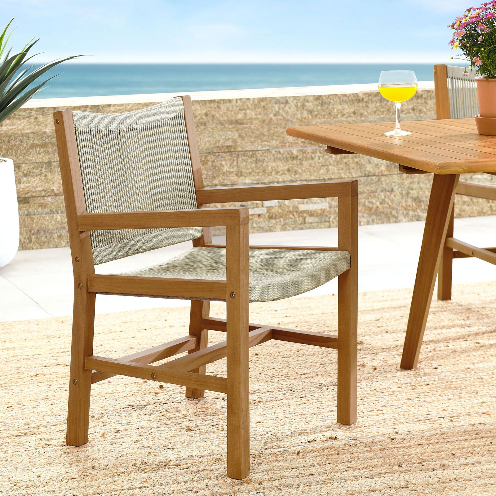 Teak and natural rope armchair styled beside a teak dining table on a bright, coastal patio || EEI-6806-NAT-NAT || front_angle_room