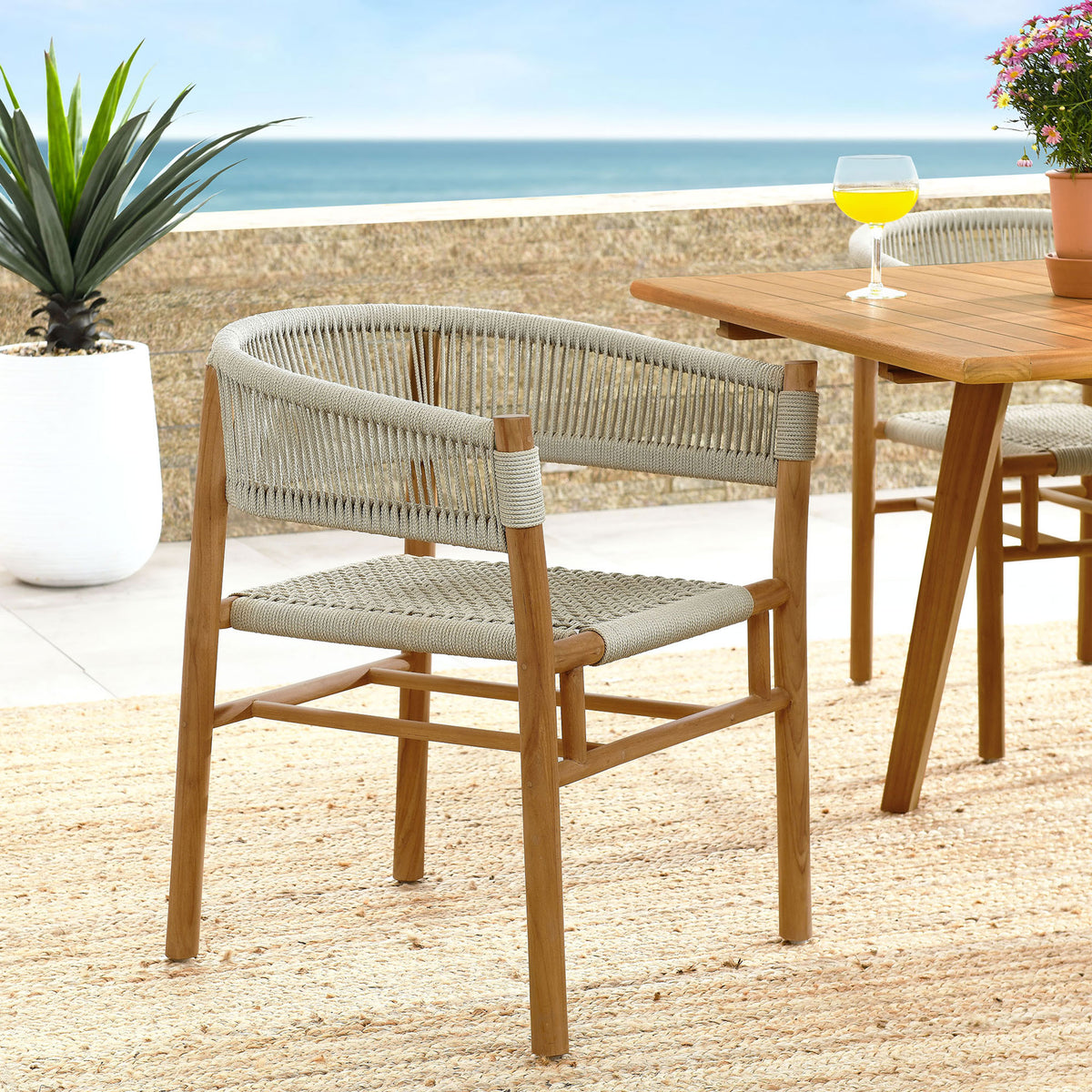 Natural rope and teak dining armchair arranged on a coastal patio with matching teak table and rug || EEI-6811-NAT-NAT || front_angle_room