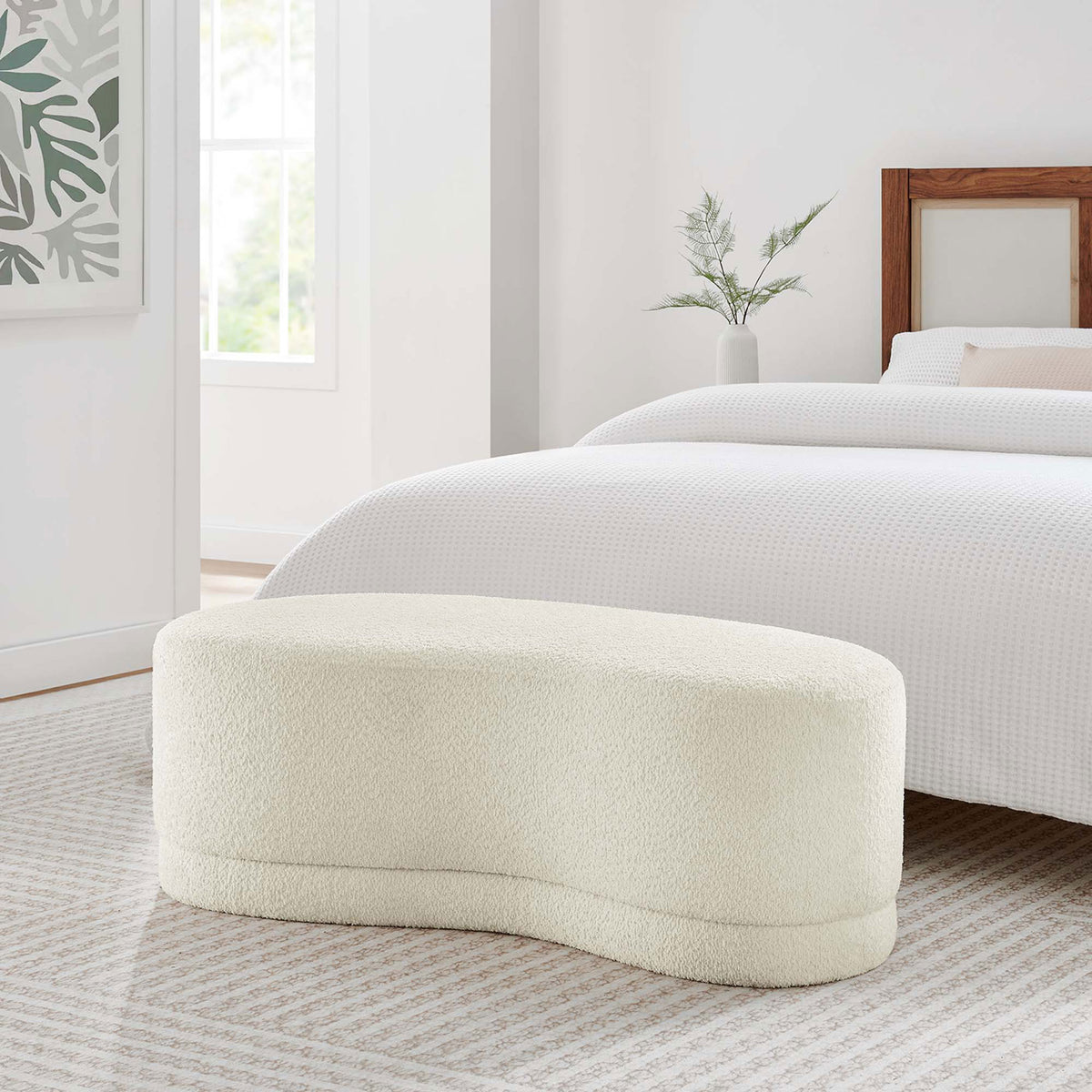 Curved cream ottoman bench sits at the foot of a bed, adding soft texture and sculptural form. || EEI-6816-CRE || front_angle_room
