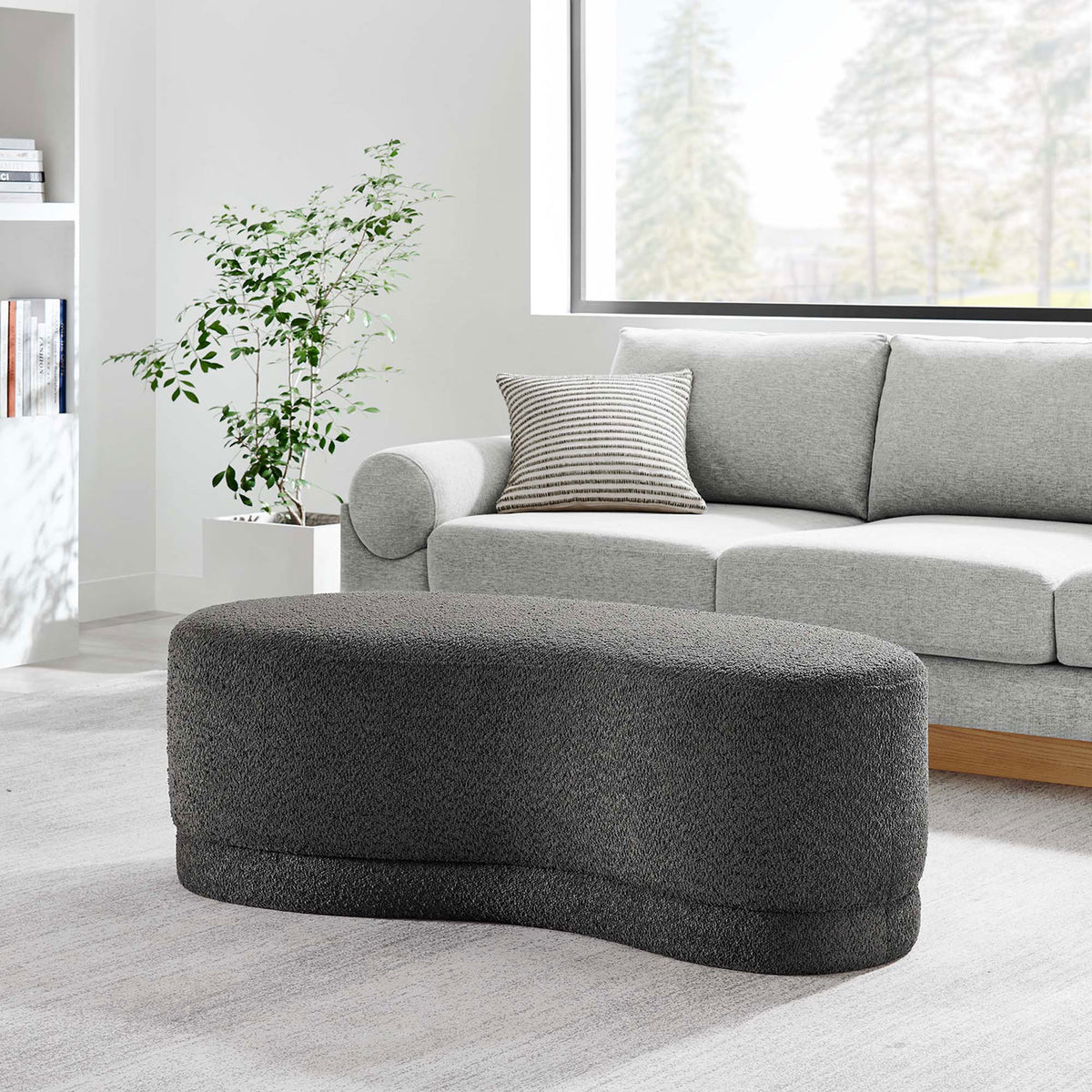 Curved dark gray ottoman bench used as a stylish coffee table in a bright modern living room. || EEI-6816-SLA || front_angle_room
