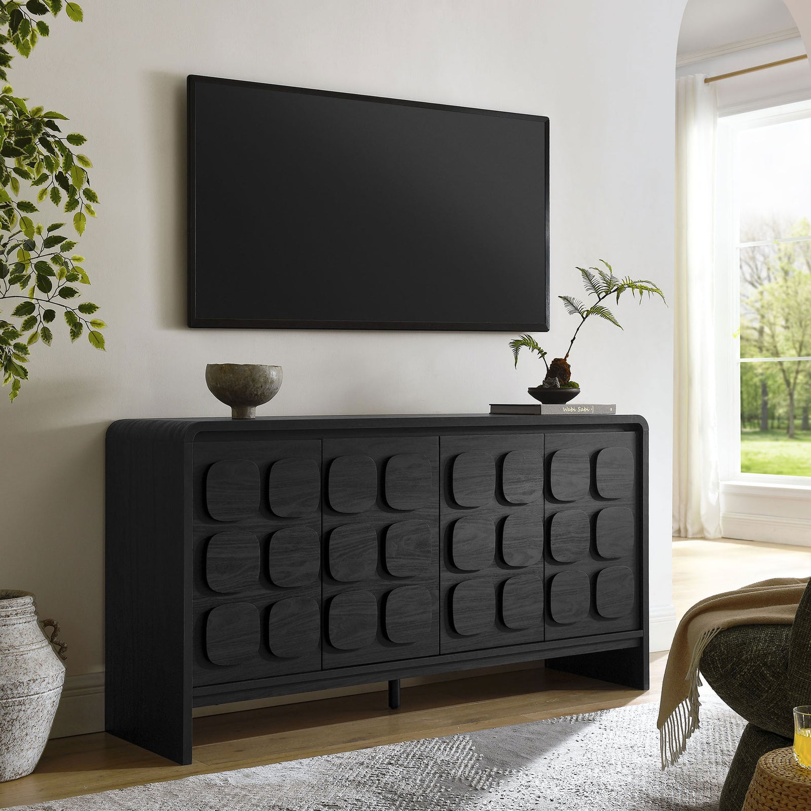 Black mid-century sideboard styled as a media console beneath a wall-mounted TV in a bright living room || EEI-6862-BLK || front_angle_room