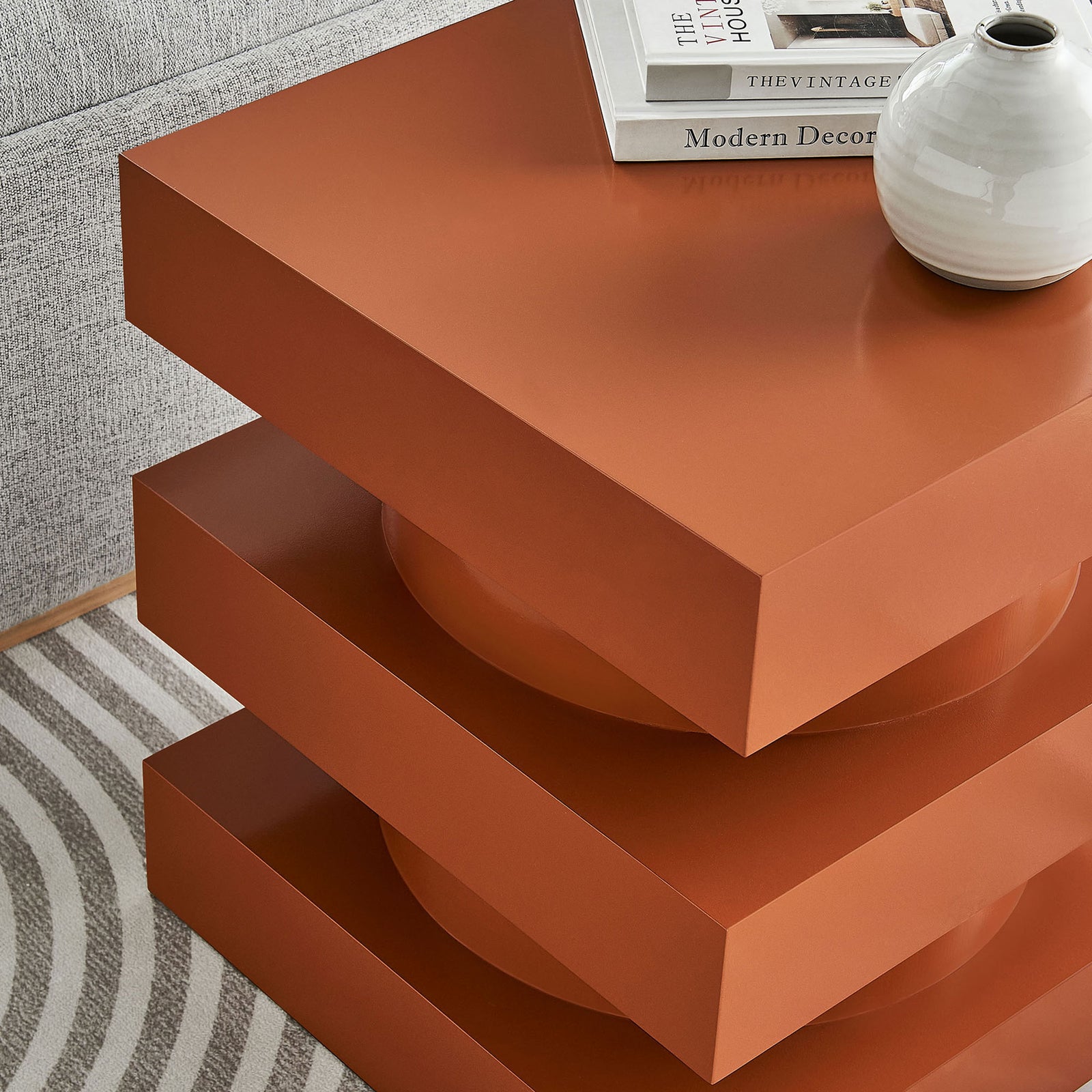 Totem end table styled with books and a vase beside a sofa, adding a warm cayenne accent to the living room. || EEI-6864-CAY || front_angle_room