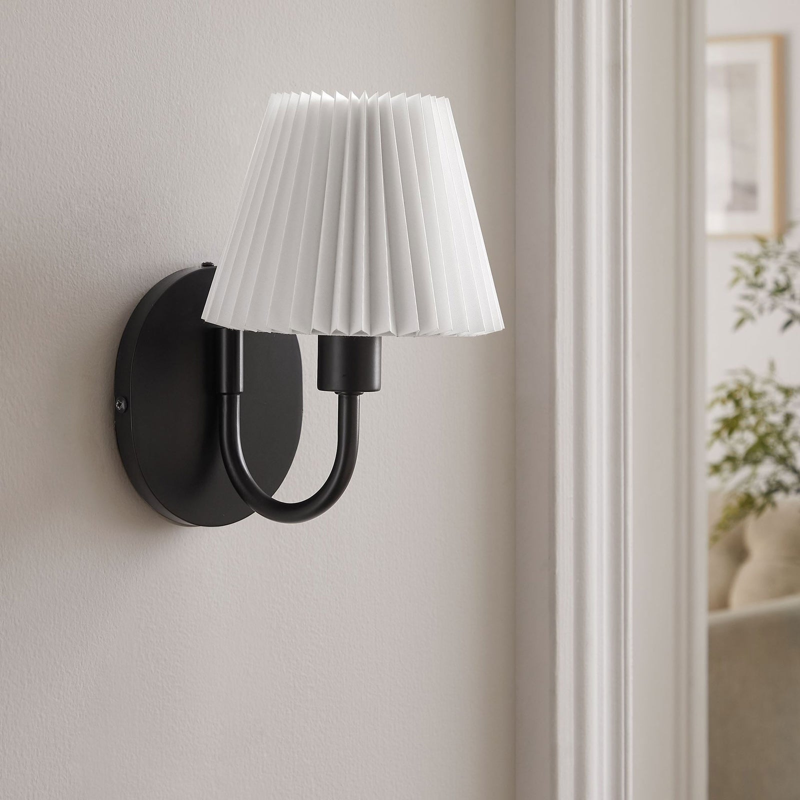 Black U-shaped wall sconce with pleated shade adds a refined modern touch to a soft, neutral living space. || EEI-6872-BLK || front_angle_room