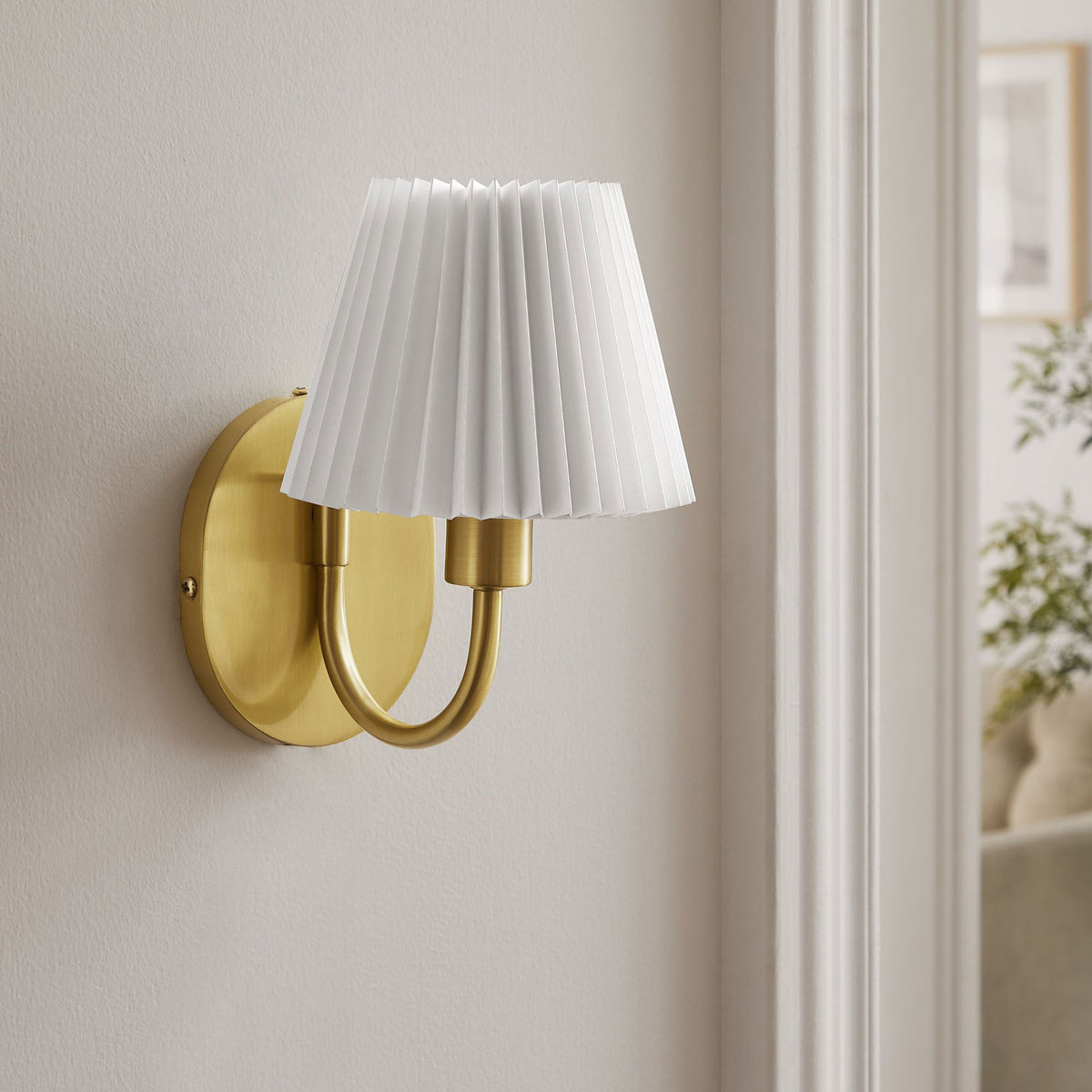 Brass U-shaped wall sconce with pleated shade adds a polished accent to a calm, neutral living space. || EEI-6872-BRA || front_angle_room