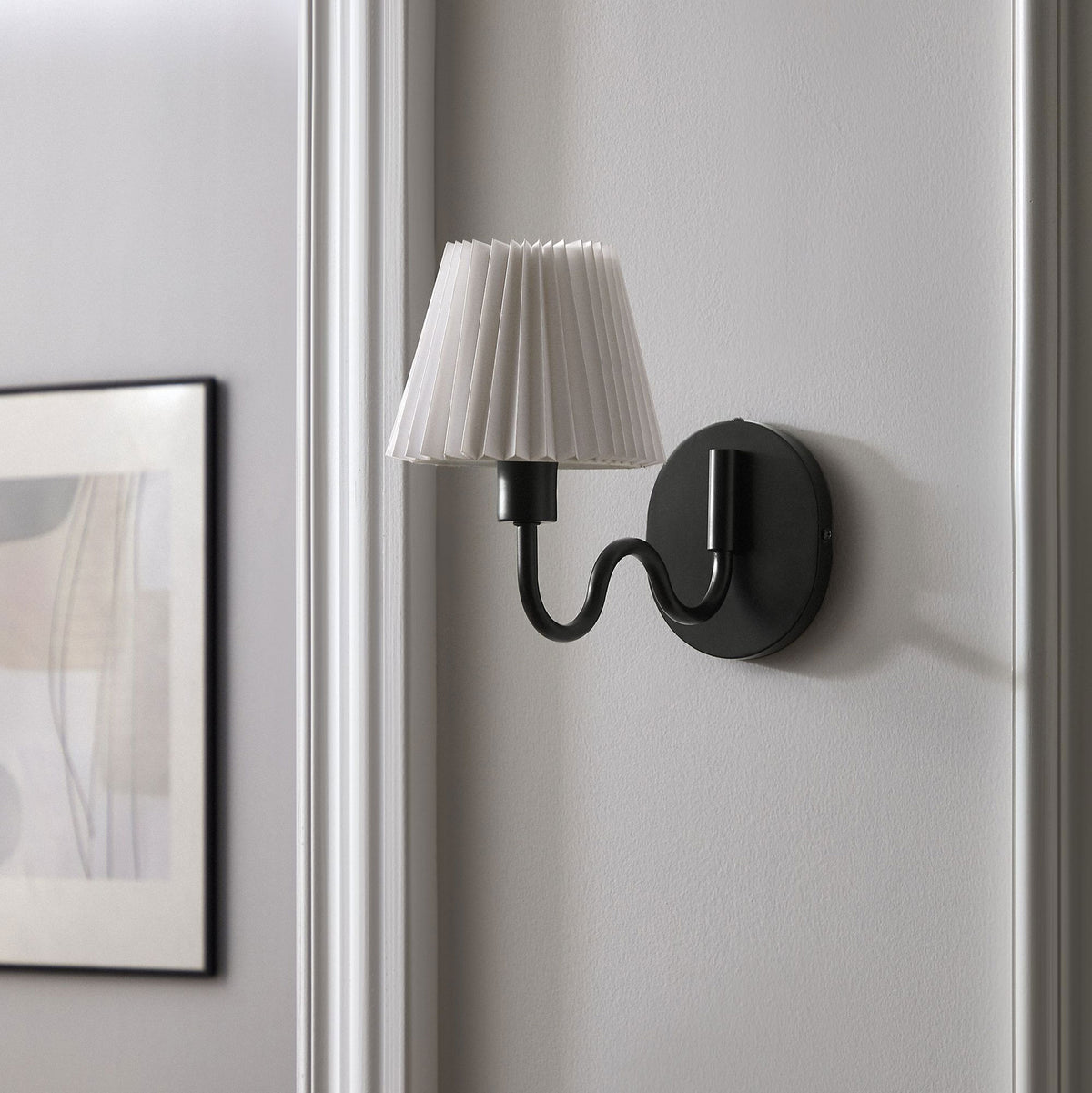 Black squiggle arm sconce with pleated shade brings modern character to a neutral hallway or entry wall. || EEI-6873-BLK || front_angle_room