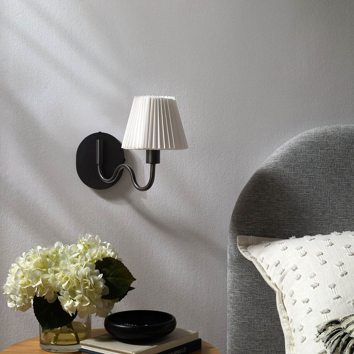 Black squiggle arm wall sconce pairs with soft bedding and florals to finish a serene modern bedroom look. || EEI-6873-BLK || front_angle_room