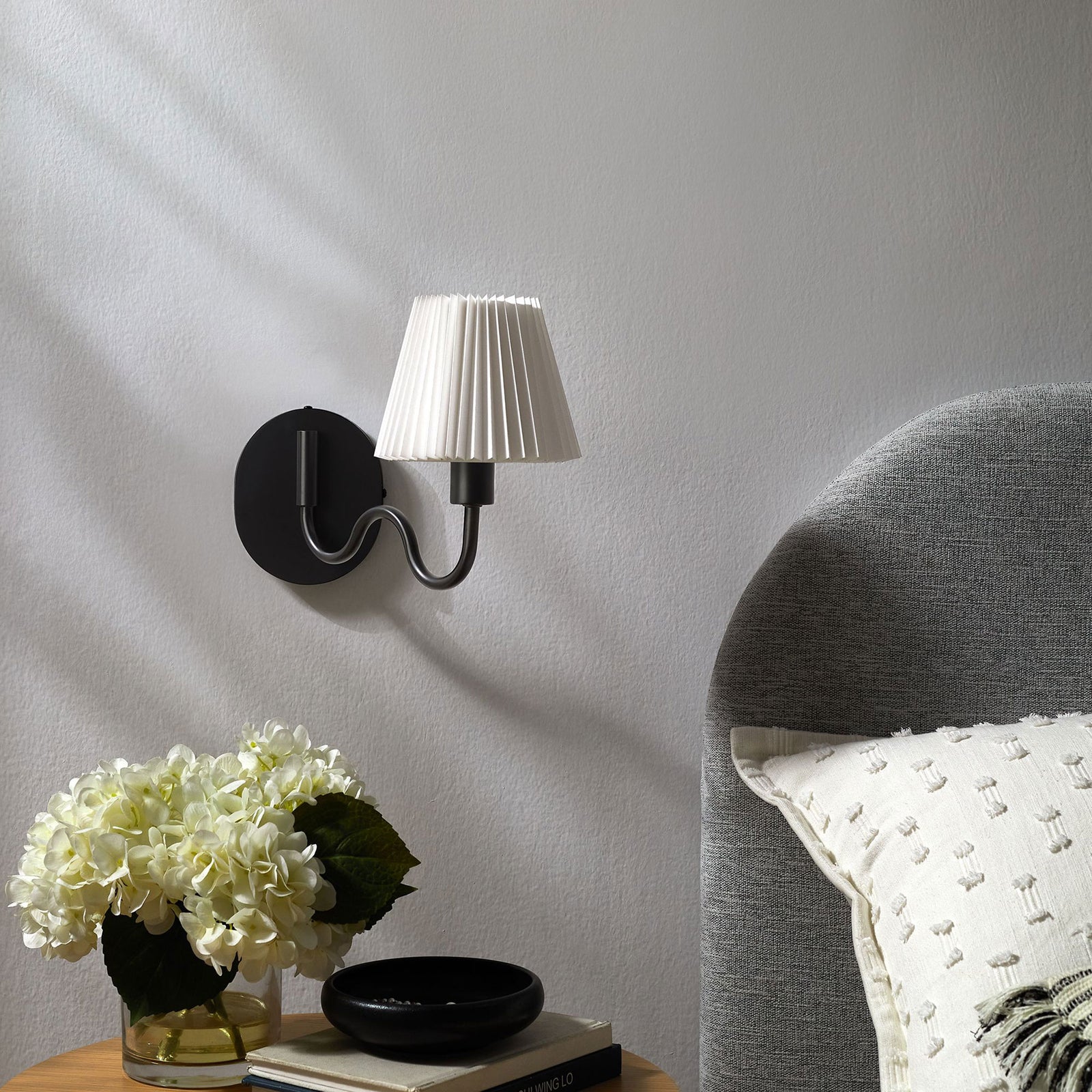 Black squiggle arm wall sconce pairs with soft bedding and florals to finish a serene modern bedroom look. || EEI-6873-BLK || front_angle_room
