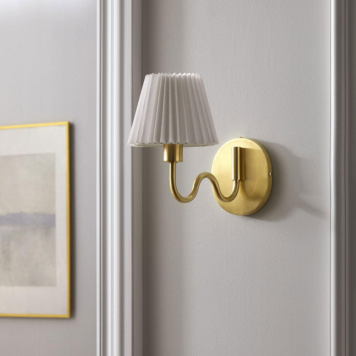 Brass squiggle arm sconce with pleated shade brings a touch of glam warmth to a clean, neutral hallway wall. || EEI-6873-BRA || front_angle_room