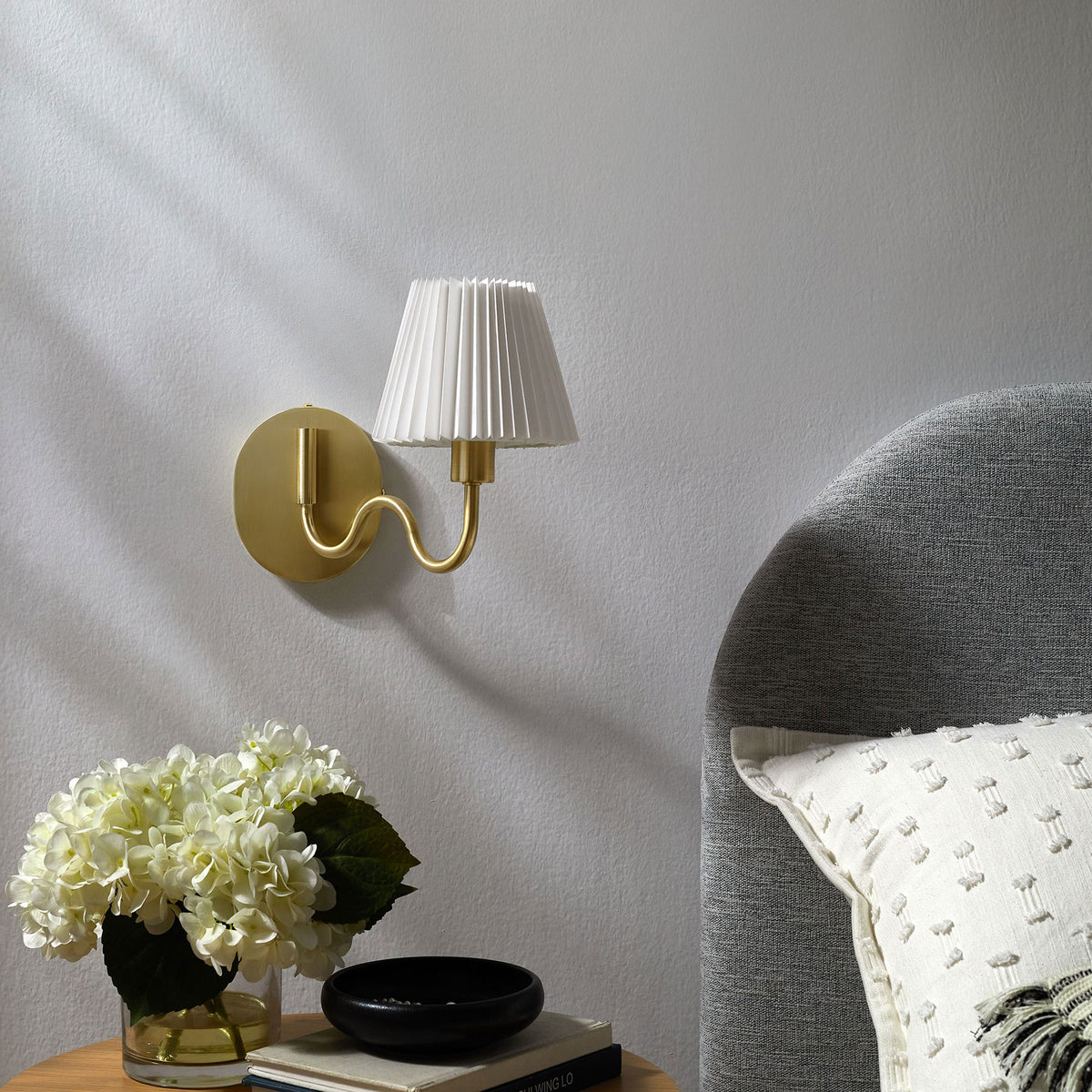 Brass squiggle arm wall sconce pairs with soft bedding and blooms to complete a light, sophisticated bedroom. || EEI-6873-BRA || front_angle_room