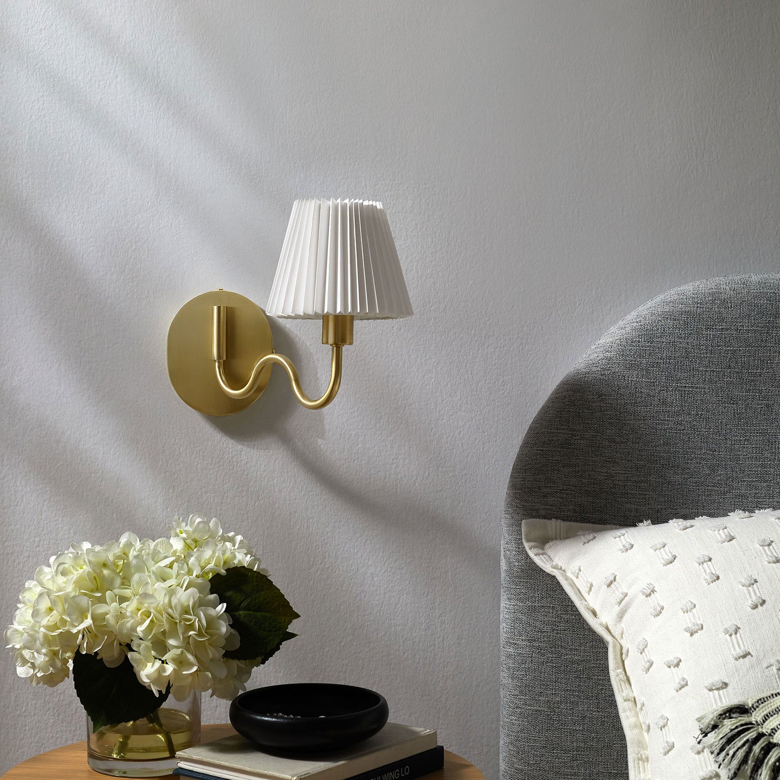 Brass squiggle arm wall sconce pairs with soft bedding and blooms to complete a light, sophisticated bedroom. || EEI-6873-BRA || front_angle_room