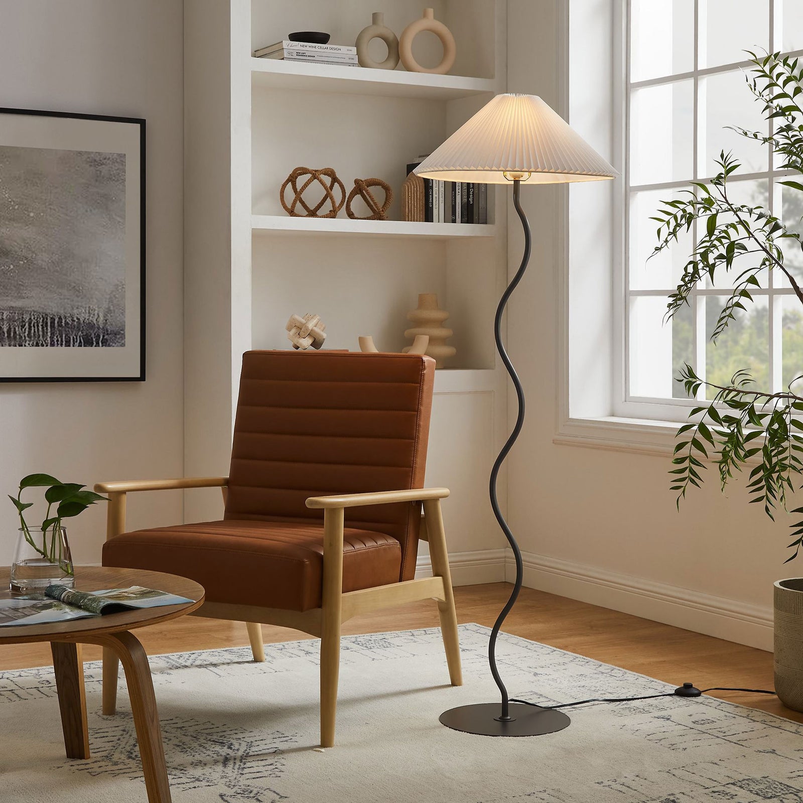 Squiggle floor lamp glowing warmly beside a cozy reading chair, creating ambient light in a stylish living room. || EEI-6877-BLK || front_on_room