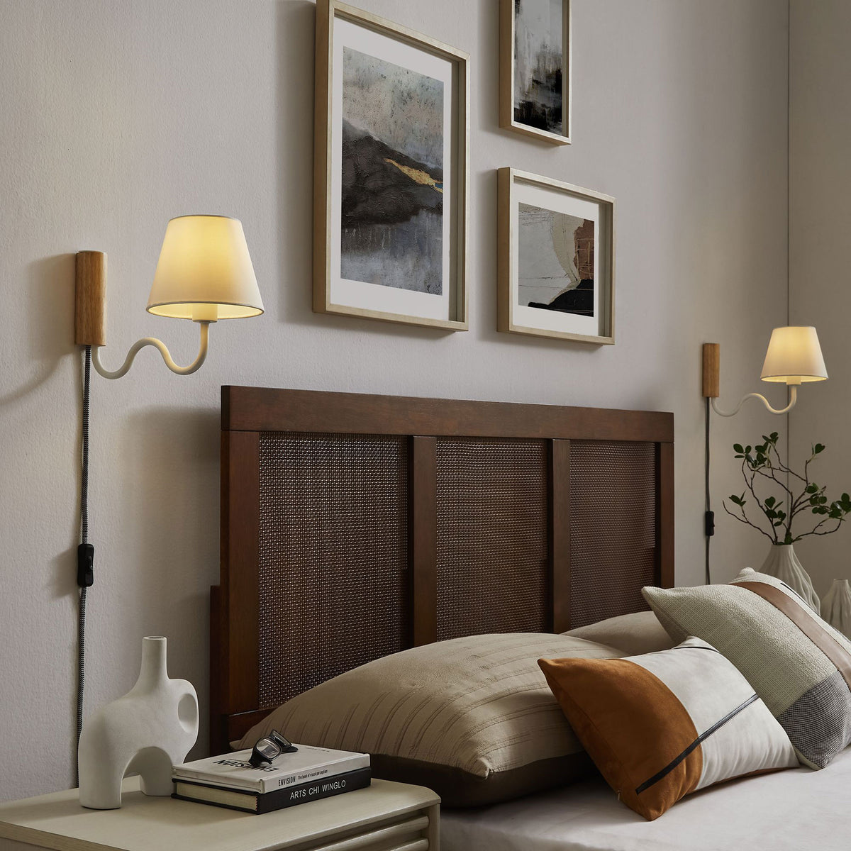 Glowing white squiggle wall sconces cast warm light over a cozy layered bed and artwork || EEI-6881-NAT-WHI || front_angle_on_room