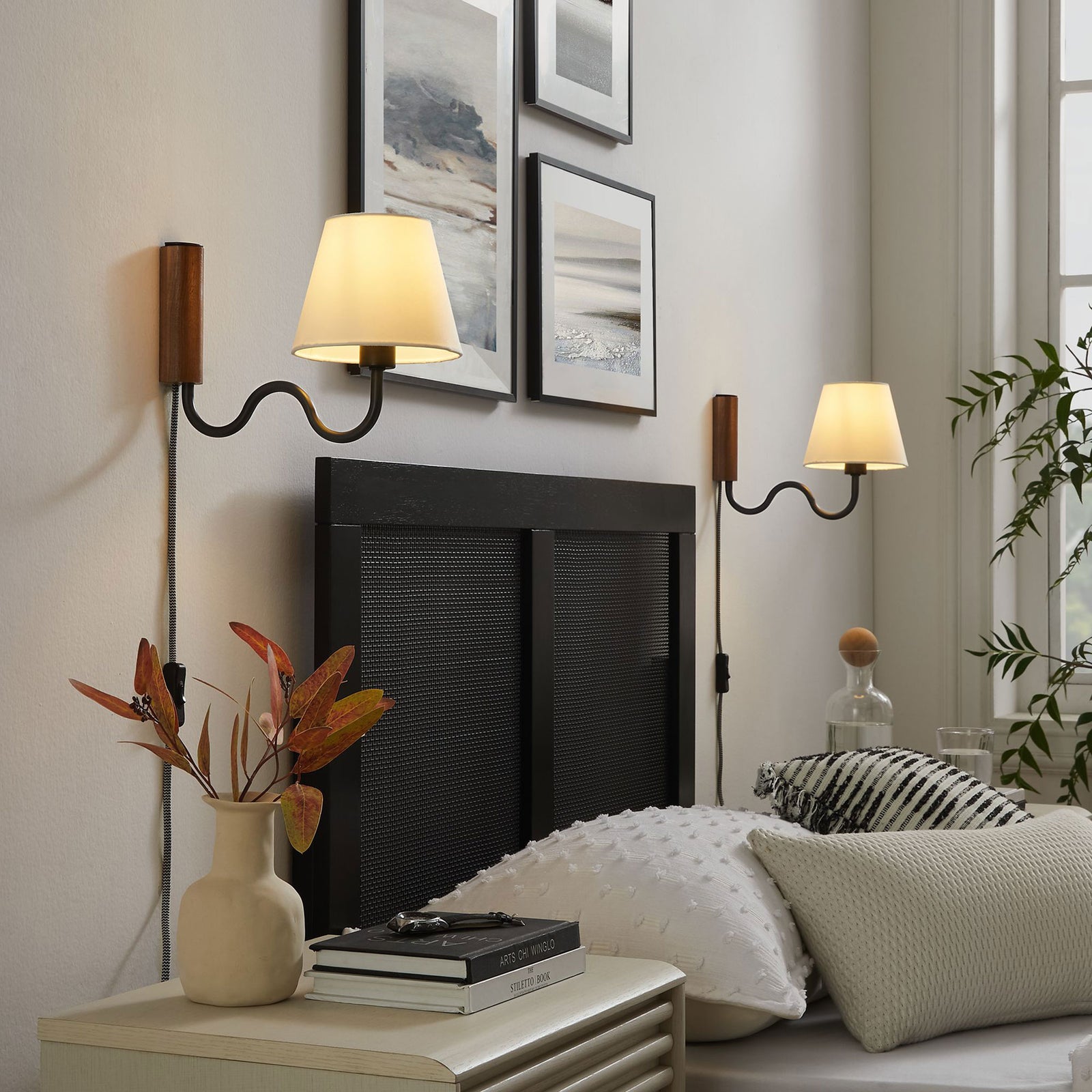 Warm light from twin squiggle arm wall sconces creates a cozy reading spot beside the bed || EEI-6881-WAL-BLK || front_angle_on_room