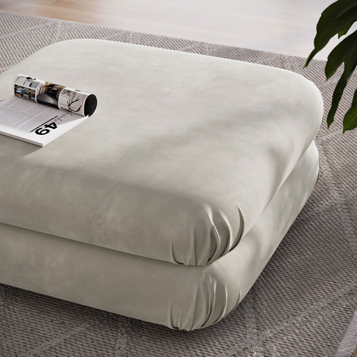Almond velvet ottoman used as a coffee table with magazine on top over a textured rug || EEI-6899-ALM || top_angle_room