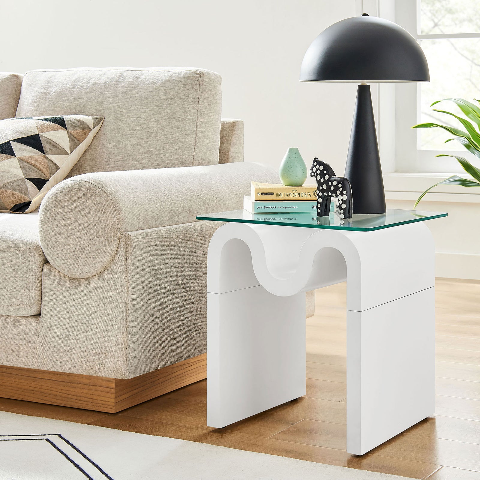 Ondine glass top side table beside a sofa, bringing playful modern curves to the living room || EEI-6902-WHI || front_angle_room