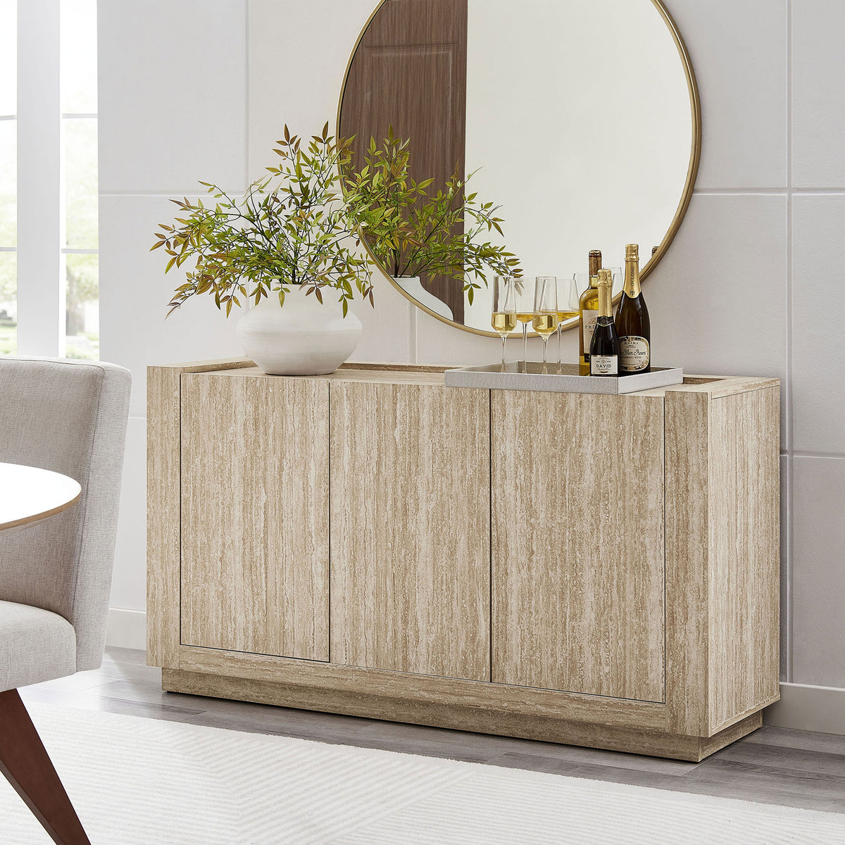 Travertine sideboard styled in a bright dining room, anchoring a round mirror and decor || EEI-6906-TRA || front_angle_room