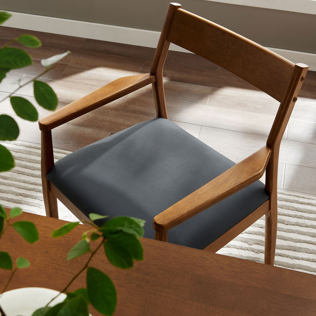 Walnut dining armchair beside a table, showing the black seat cushion and slender wooden arms. || EEI-6915-WAL-BLK || detail_room