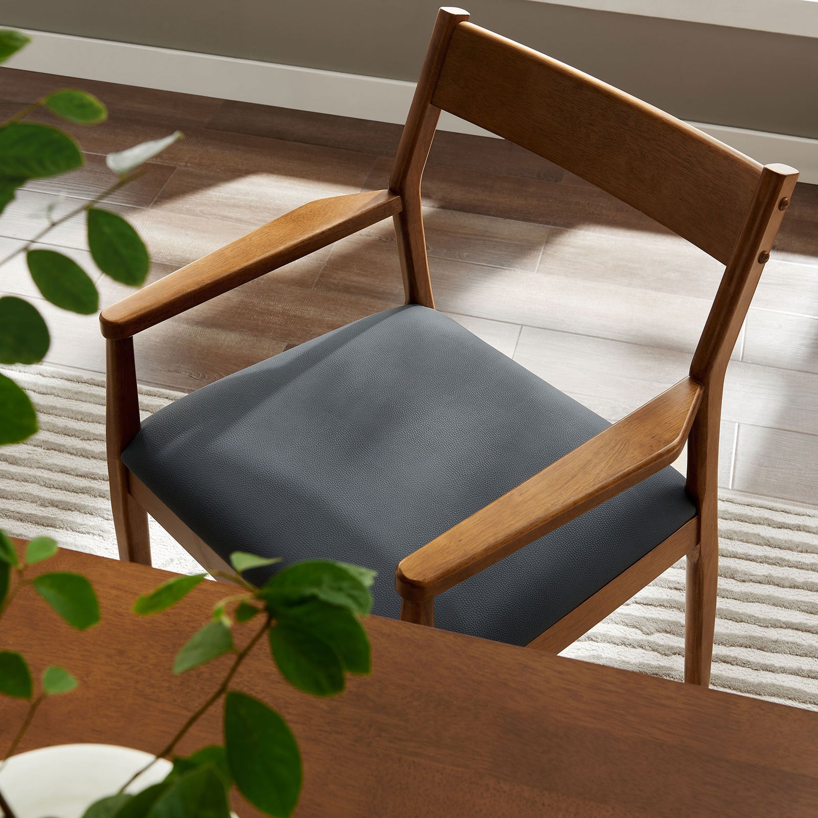 Walnut dining armchair beside a table, showing the black seat cushion and slender wooden arms. || EEI-6915-WAL-BLK || detail_room