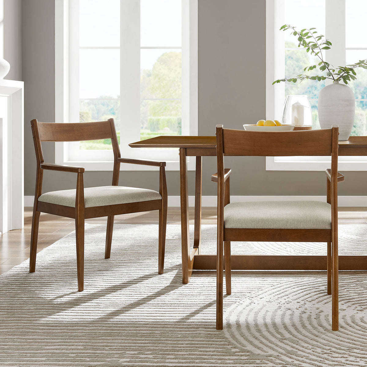 Pair of walnut dining armchairs with beige seats arranged around a rectangular wood table in a bright dining room || EEI-6916-WAL-HEB || front_angle_multi_room