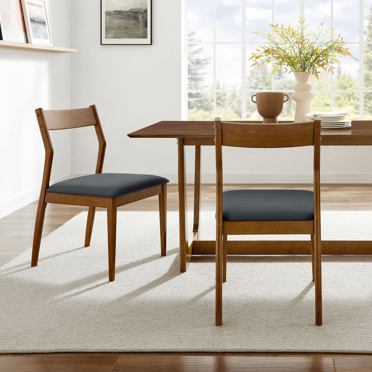Pair of walnut dining chairs with black vegan leather seats around a modern dining table. || EEI-6917-WAL-BLK || front_angle_multi_room