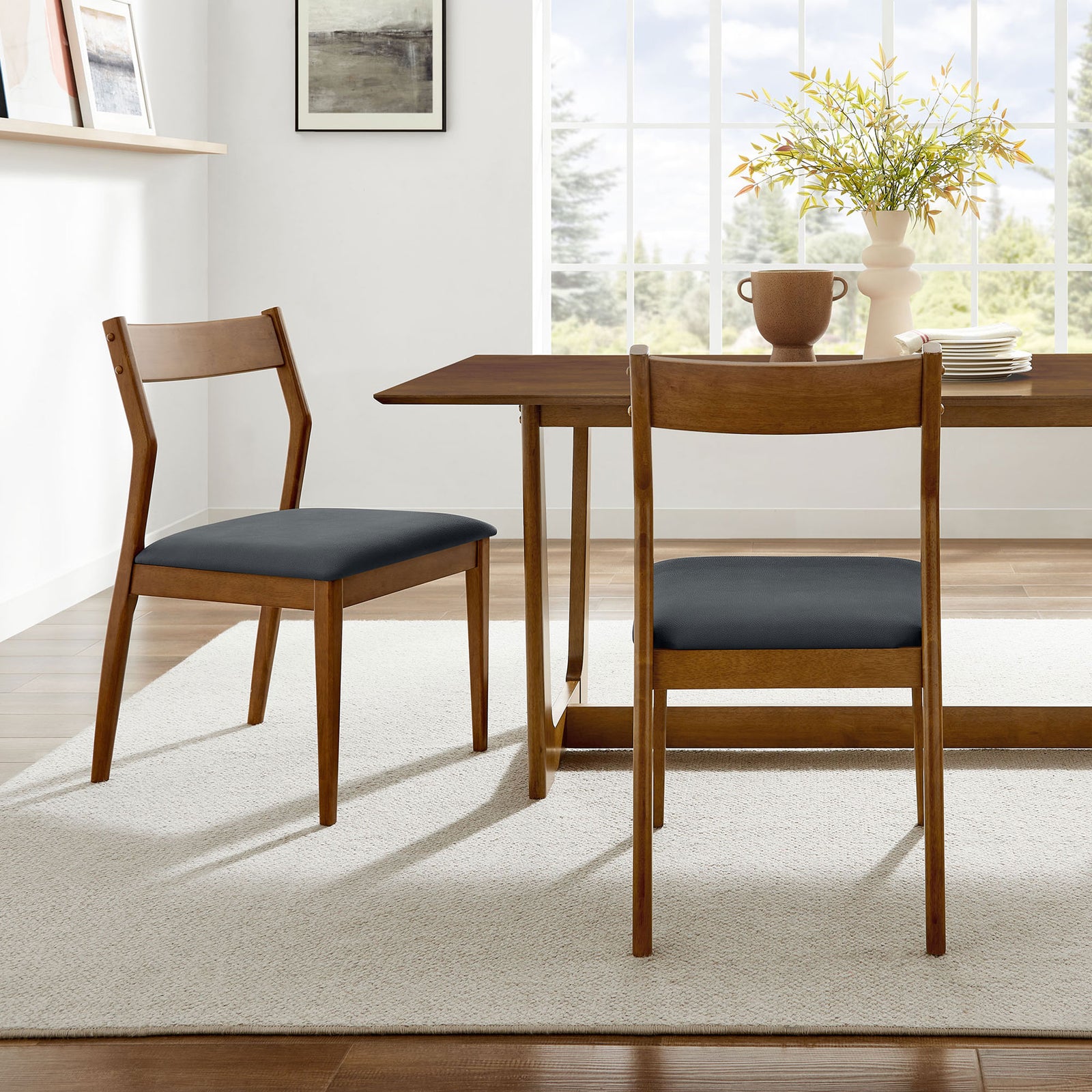 Pair of walnut dining chairs with black vegan leather seats around a modern dining table. || EEI-6917-WAL-BLK || front_angle_multi_room