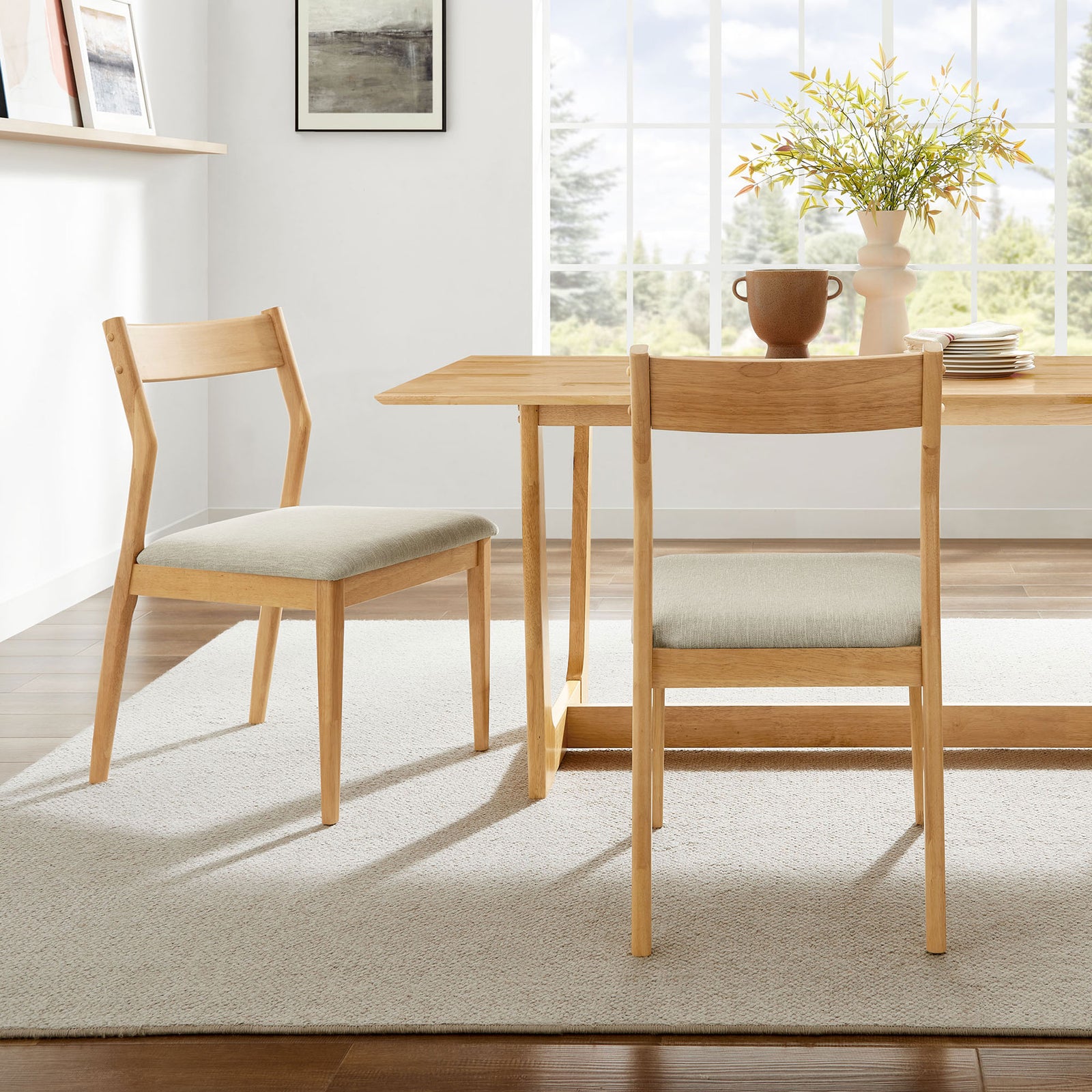 Pair of natural wood dining chairs with beige cushions arranged around a bright contemporary table || EEI-6918-NAT-HEB || front_multi_room