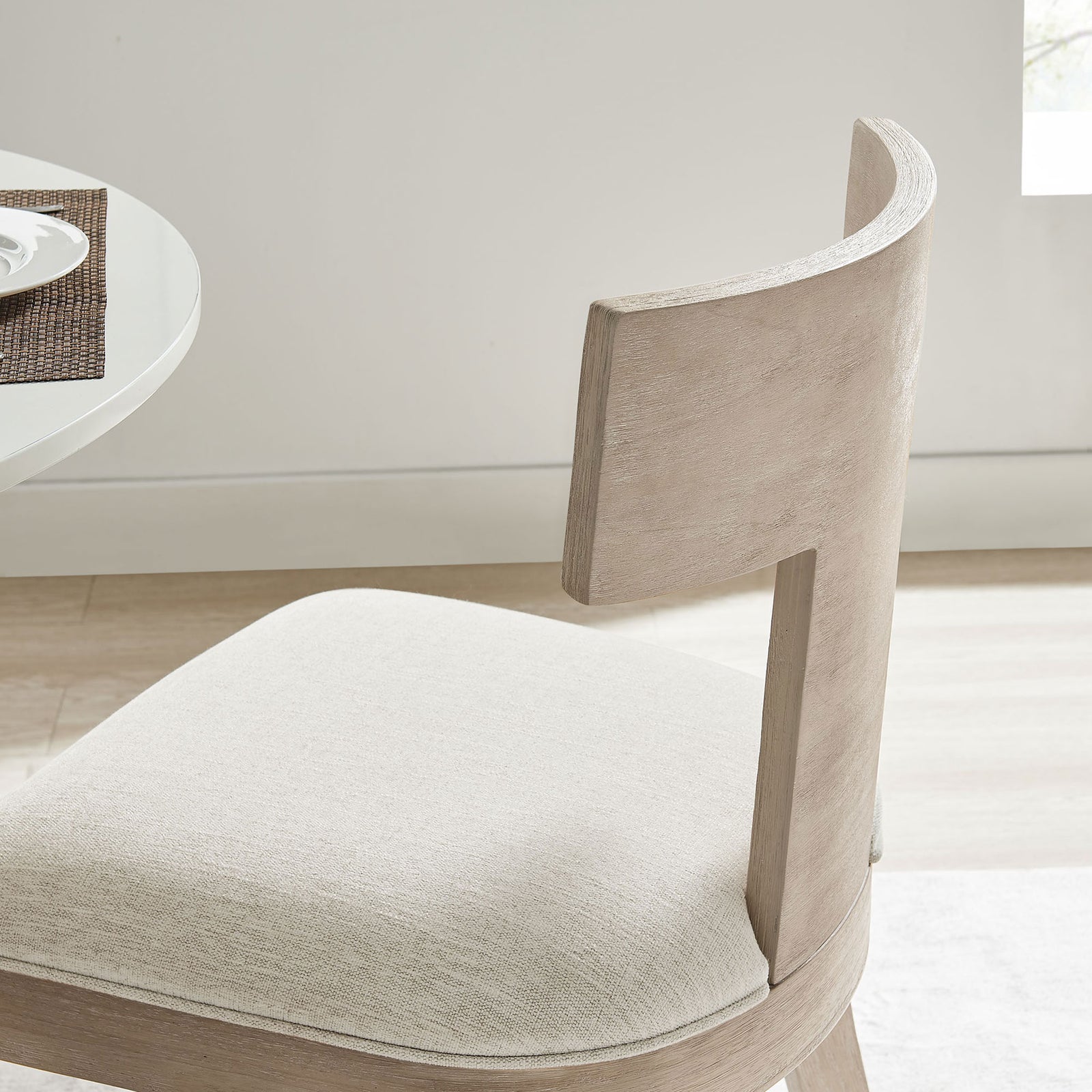 Upholstered ivory seat and curved wood back of Peregrine dining chair styled in a modern dining space || EEI-6923-NAT-HEI || detail_room