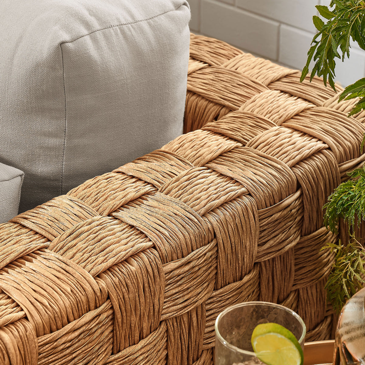 Arm of the Thames natural rattan armchair with light gray cushion beside greenery and a drink tray || EEI-6925-NAT-LGR || detail_room