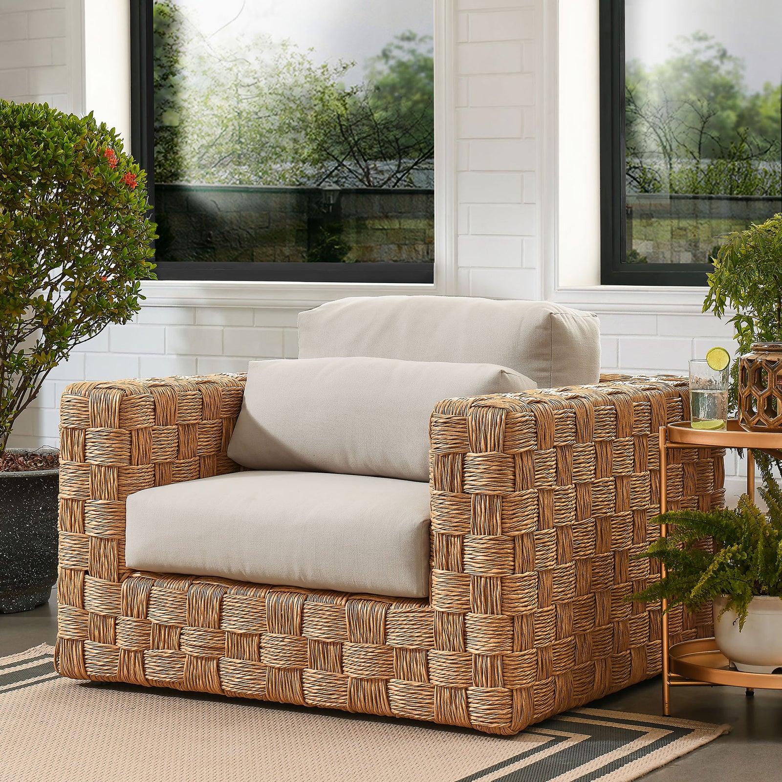 Thames natural rattan outdoor armchair with light gray cushions styled on a patio with greenery || EEI-6925-NAT-LGR || front_angle_room