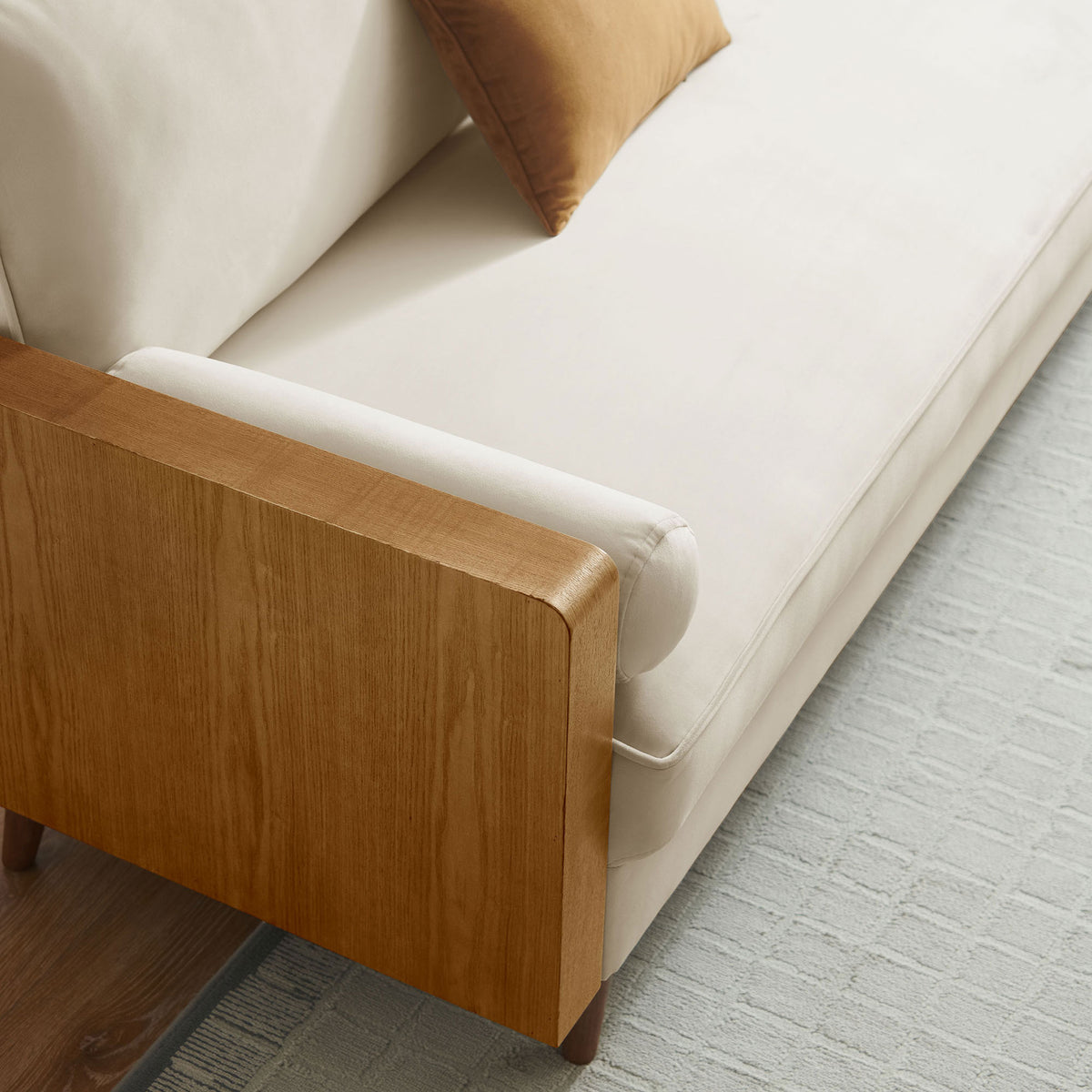 Cream velvet sofa arm and bolster sit over a textured rug with a warm caramel accent pillow || EEI-6944-WAL-ALA || detail_room