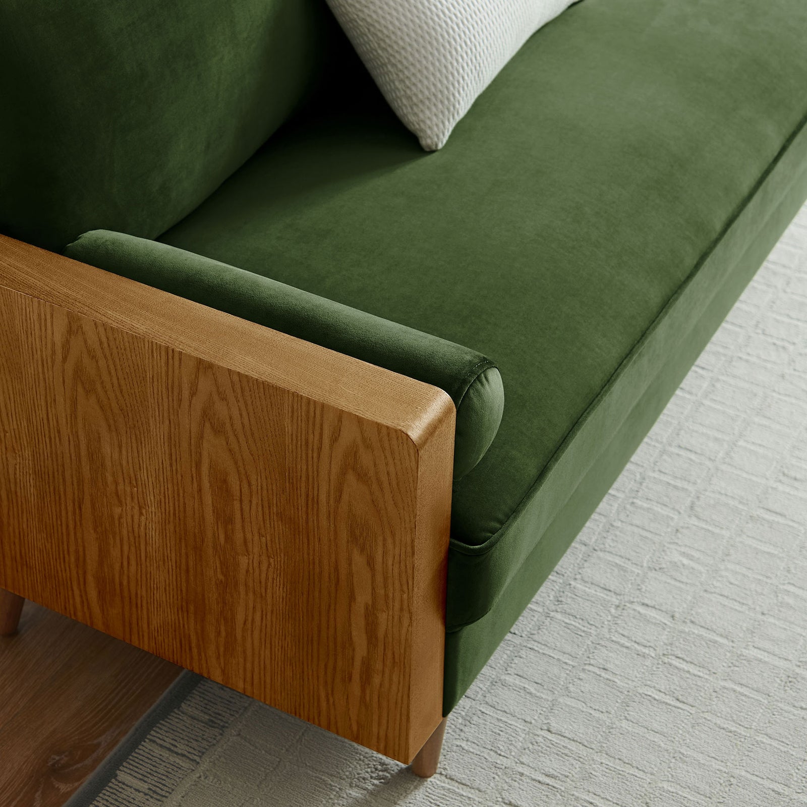 Green velvet sofa corner styled with a textured accent pillow and light rug in a bright living room || EEI-6944-WAL-MOG || detail_room