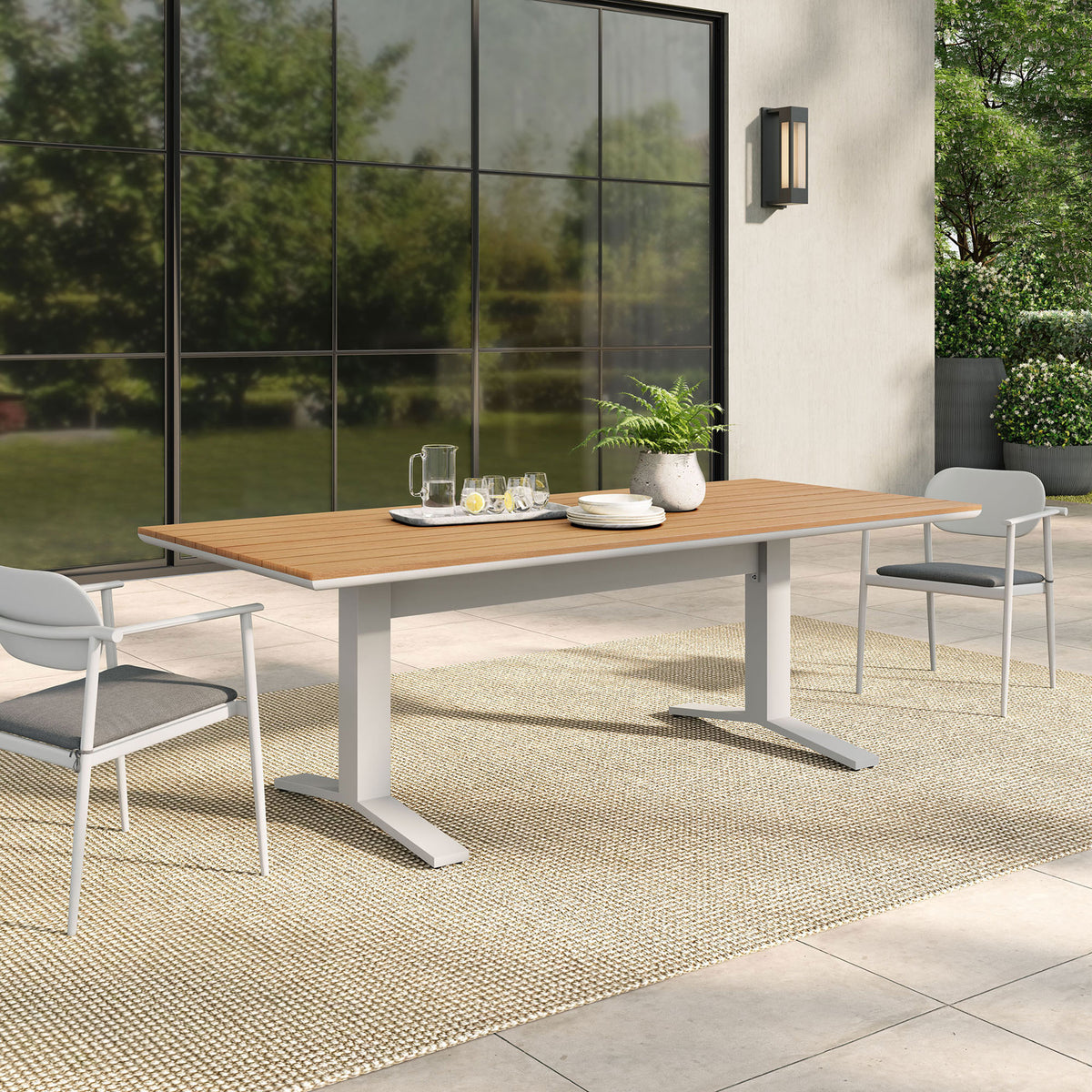 Gavelston natural outdoor dining table arranged on a bright patio with coordinating chairs and greenery. || EEI-6948-NAT-WHI || front_angle_room
