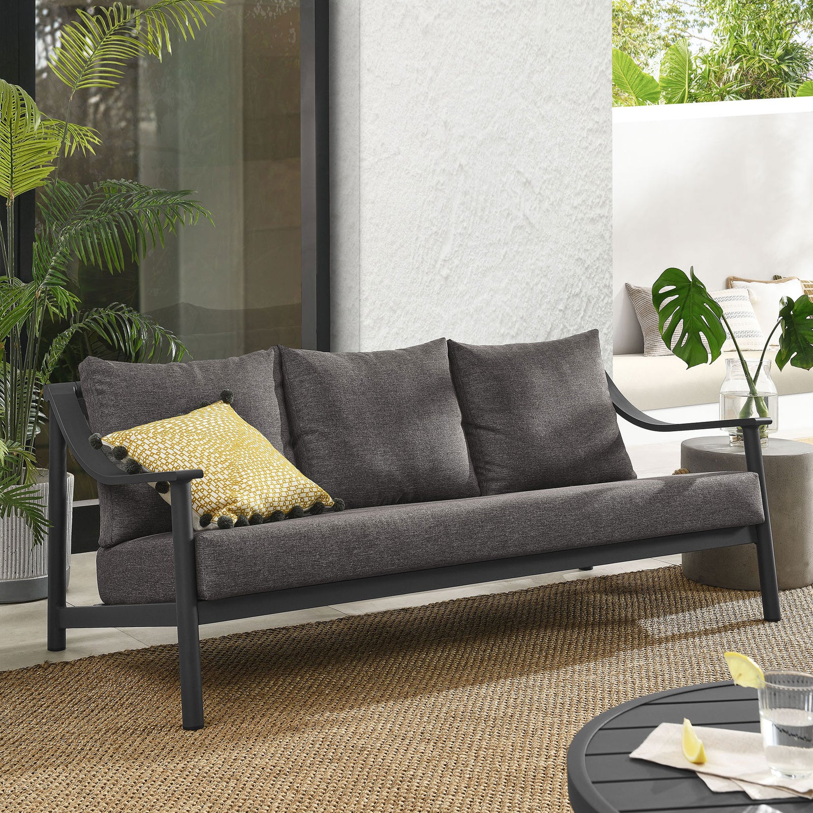 Graphite outdoor sofa styled on a sunlit patio with plush cushions and sleek charcoal aluminum frame || EEI-6977-CAR-GPH || front_angle_room