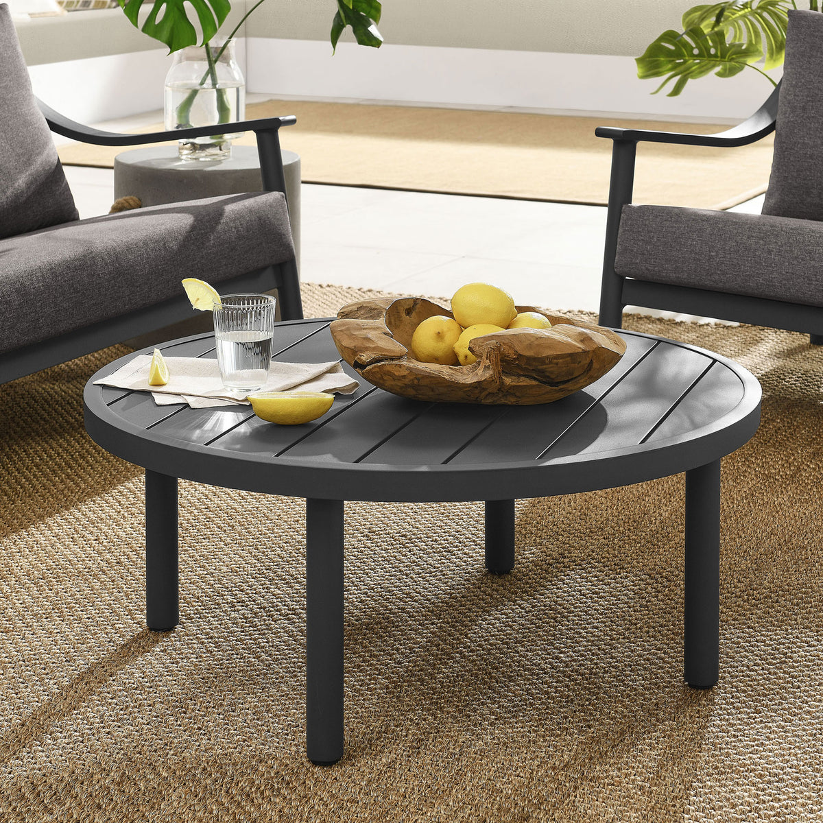 Round graphite outdoor coffee table anchoring a modern patio lounge set on woven rug || EEI-6978-GPH || front_angle_room
