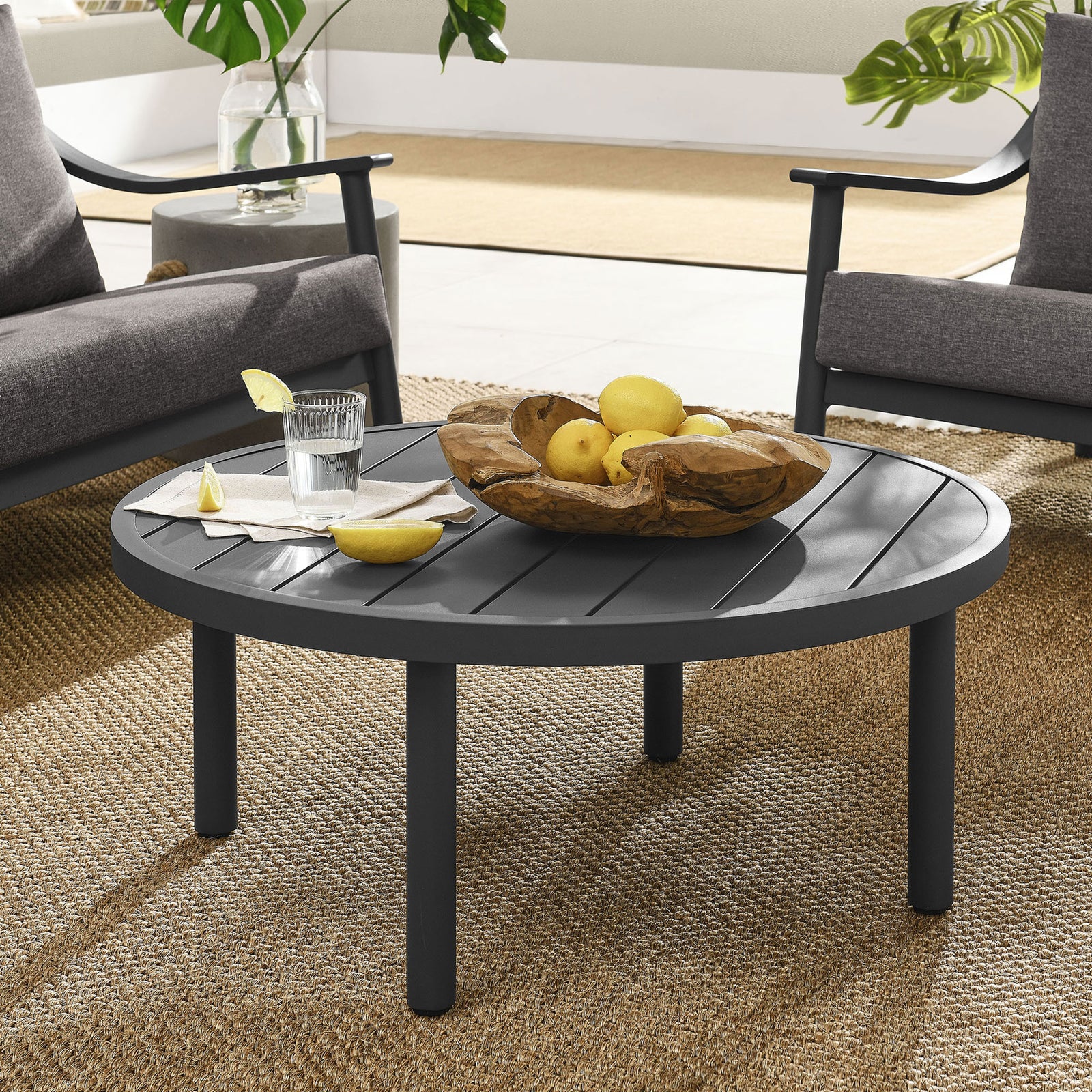 Round graphite outdoor coffee table anchoring a modern patio lounge set on woven rug || EEI-6978-GPH || front_angle_room