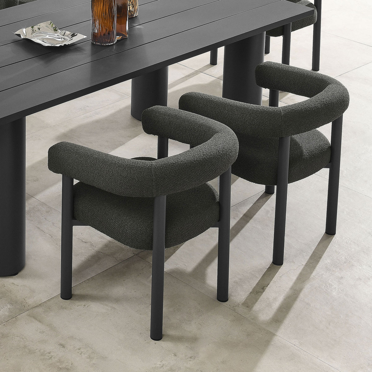 Pair of charcoal graphite armchairs arranged at a modern outdoor dining table on a light stone patio || EEI-6979-CHA-GPH || front_angle_multi_room