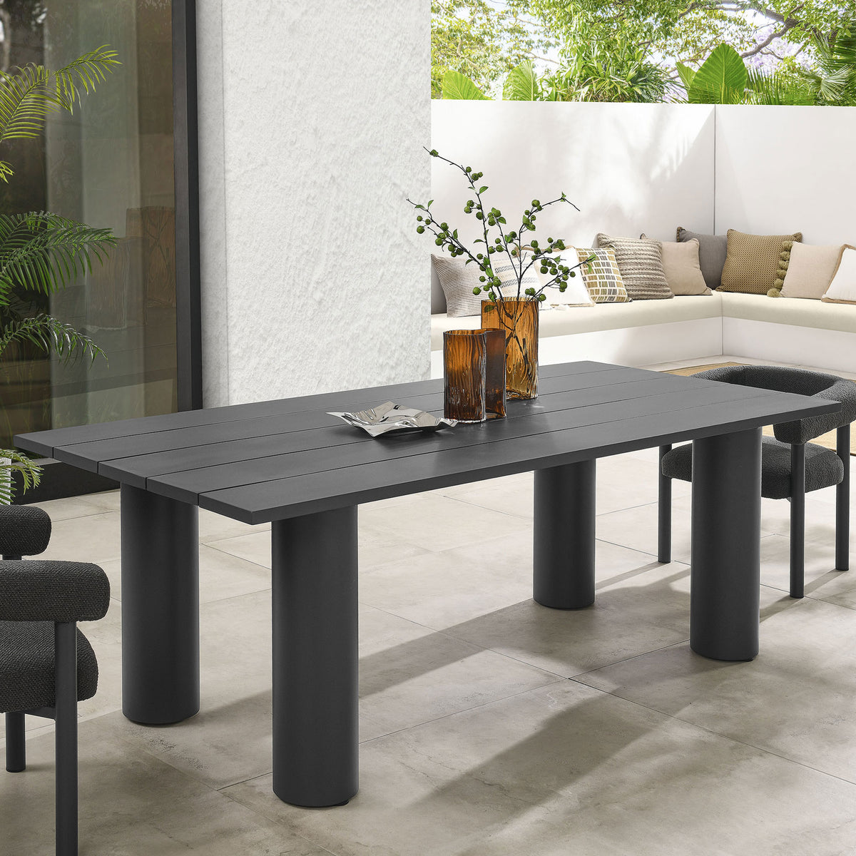 Graphite aluminum patio dining table styled with neutral chairs and amber vases in a lush modern outdoor lounge || EEI-6980-GPH || front_angle_room