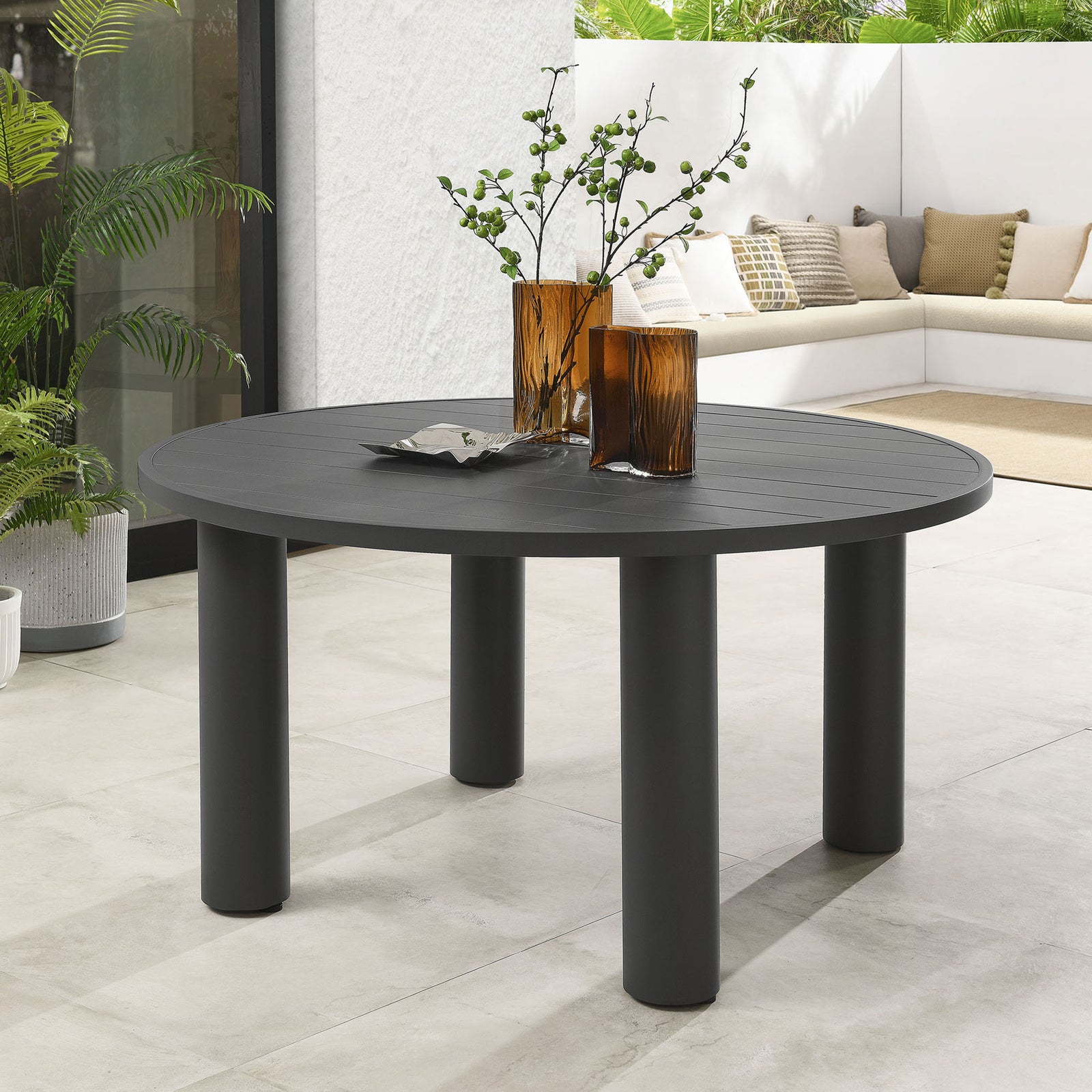 Graphite round aluminum dining table styled with warm amber vases and modern chairs on a sunlit outdoor terrace || EEI-6981-GPH || front_angle_room